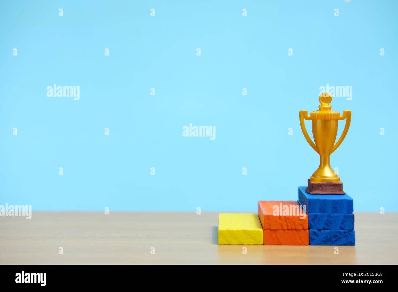 Golden trophy standing at colorful podium on wooden table Stock Photo