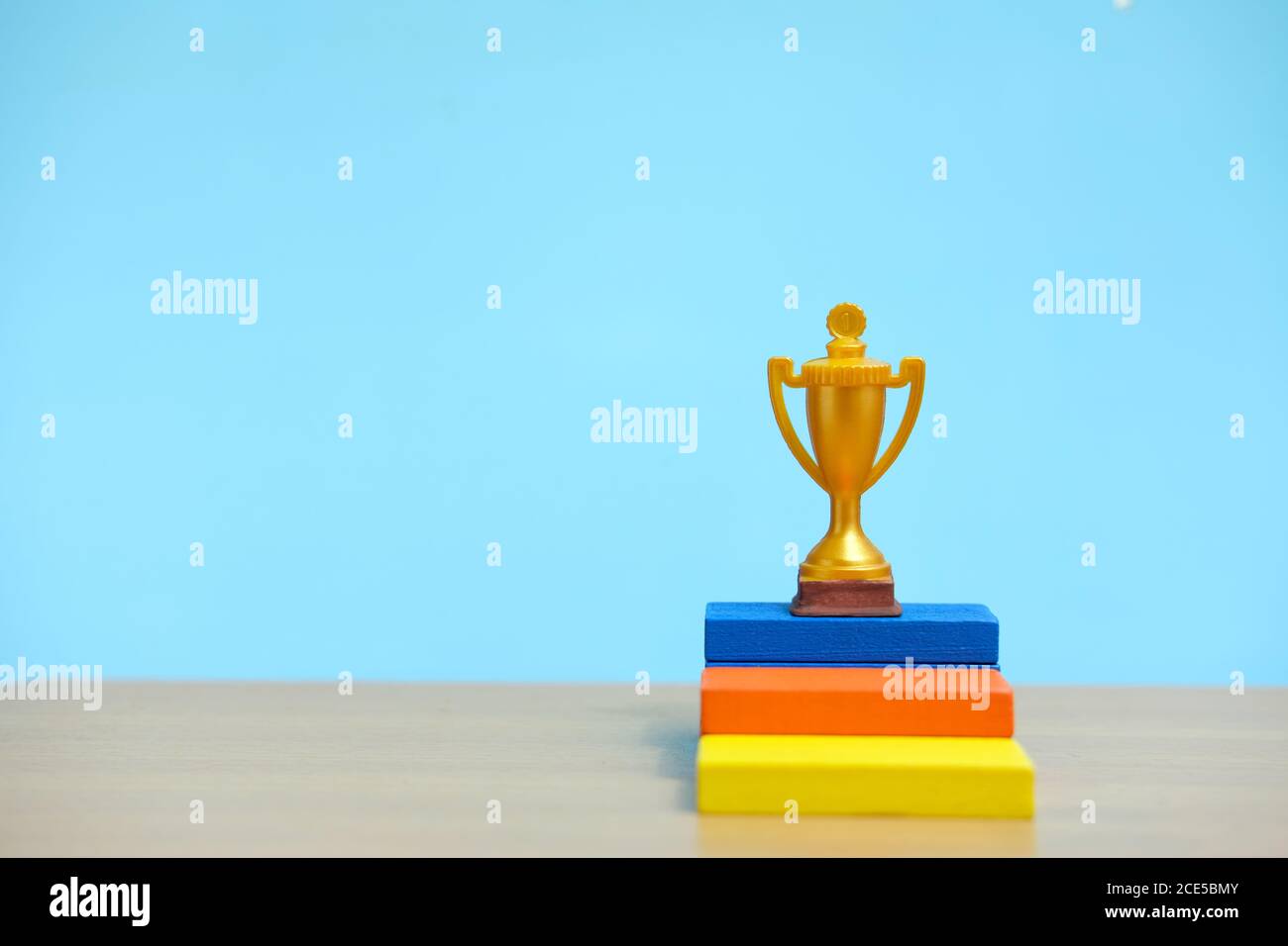 Golden trophy standing at colorful podium on wooden table Stock Photo