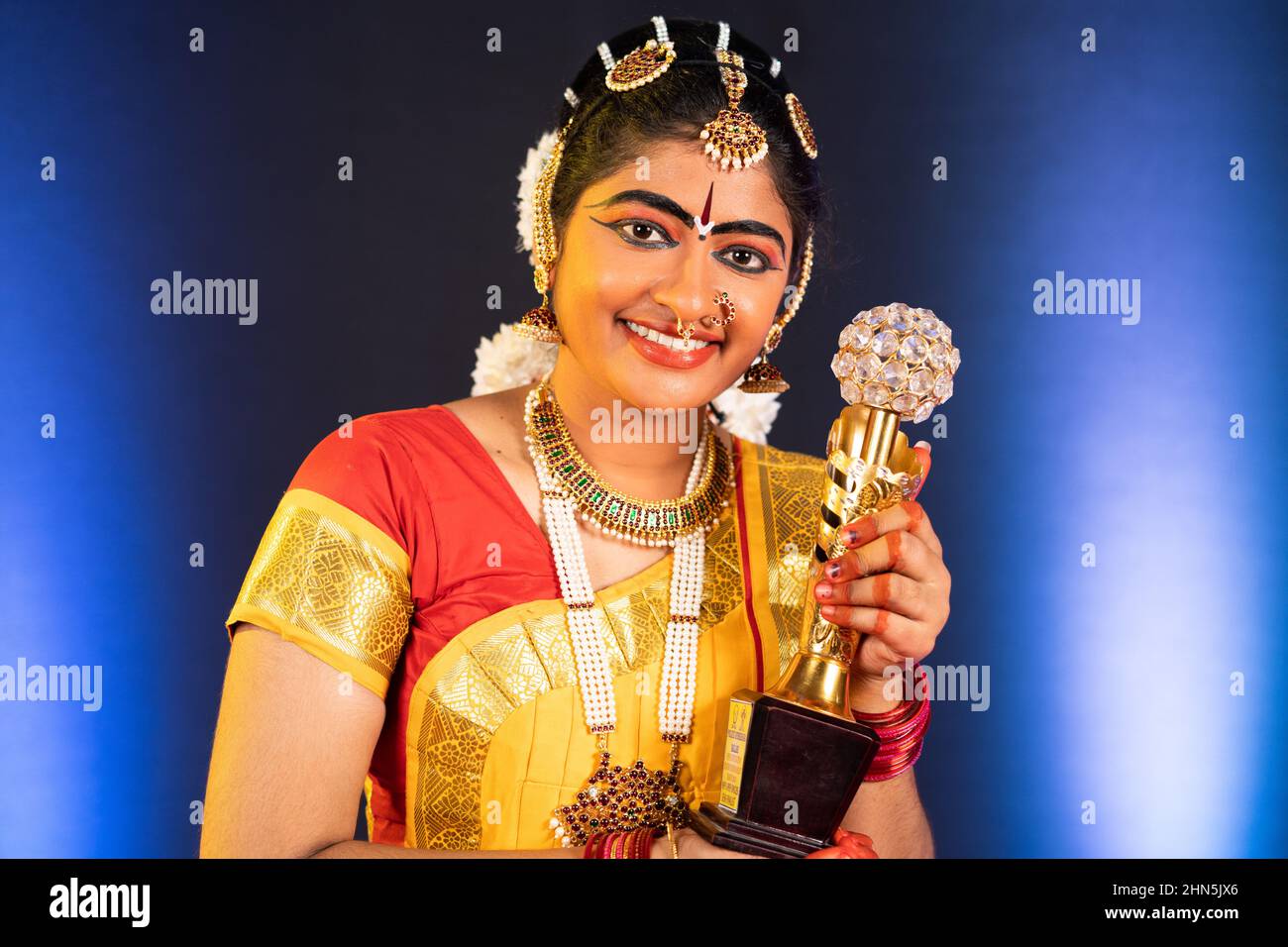 Happy smiling bharatanatyam dancer showing winner trophy by looking at camera - concept of successful, achievement, proud and indian culture Stock Photo