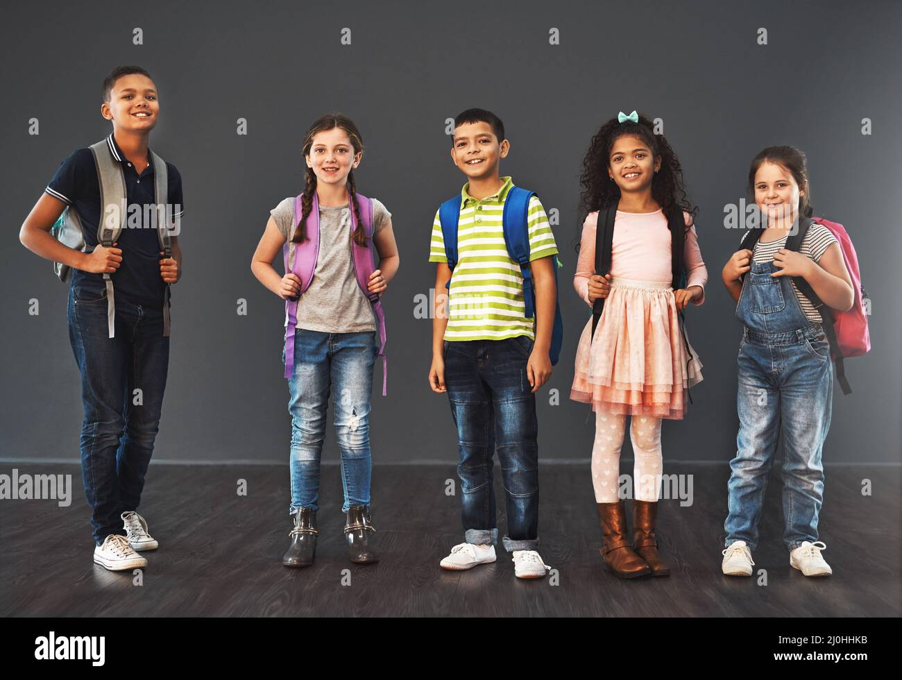 Little people, big day. Studio portrait of a diverse group of kids carrying their school backpacks against a gray background. Stock Photo