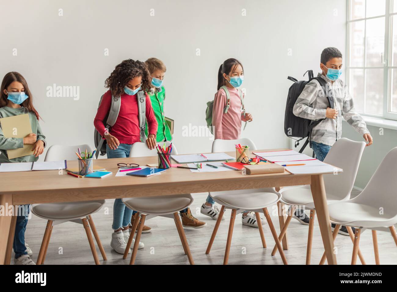 Diverse School Kids With Backpacks Wearing Face Masks Entering Classroom Stock Photo