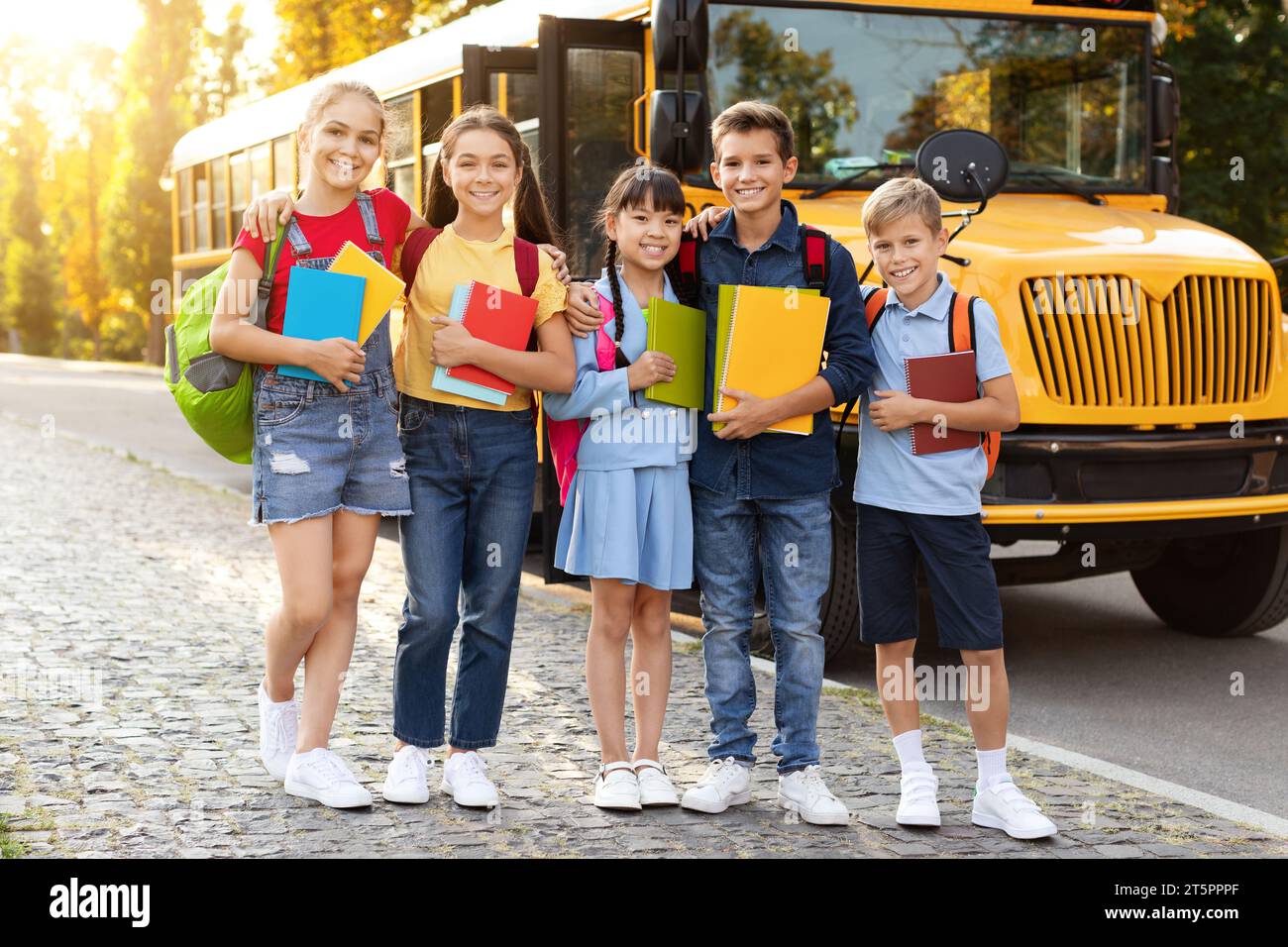 Diverse group of kids standing outside by yellow school bus, Stock Photo