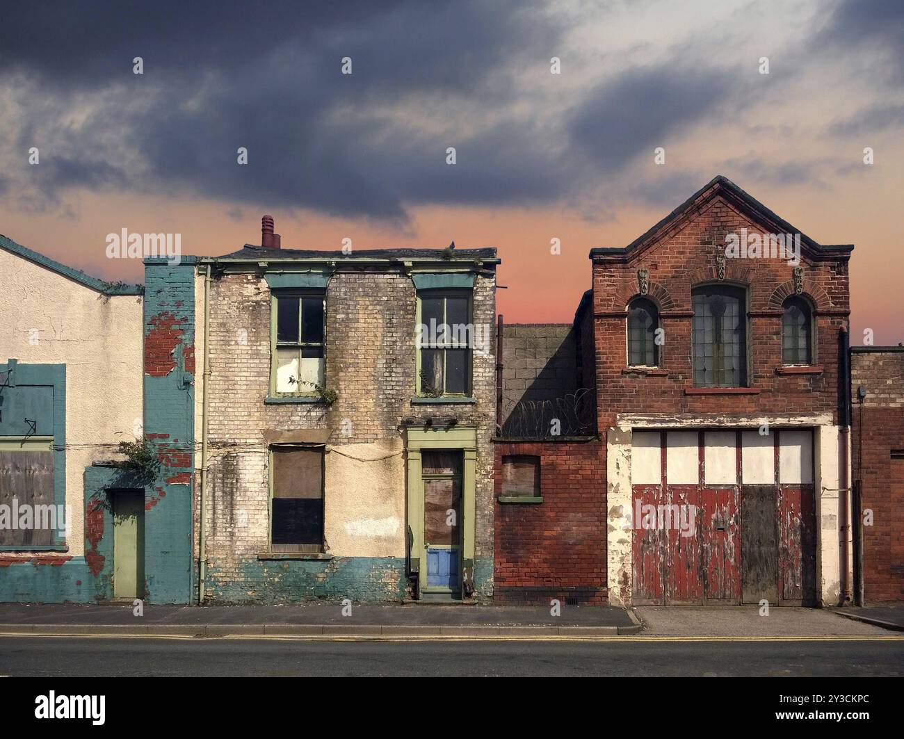 A deserted street of old abandoned ruined houses with bright peeling paint and crumbling brickwork in evening sunlight against a bright cloudy sunset Stock Photo