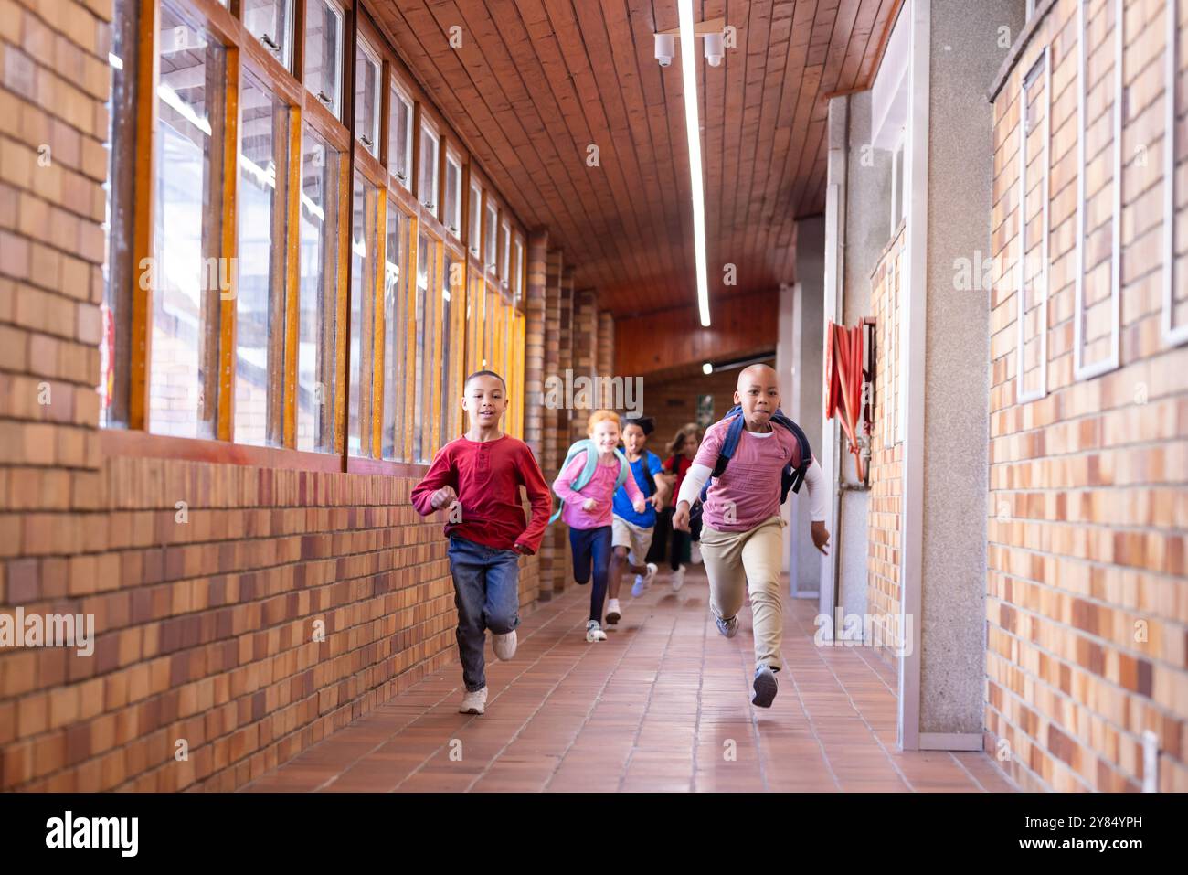 Running down school hallway, diverse children with backpacks enjoying recess time Stock Photo