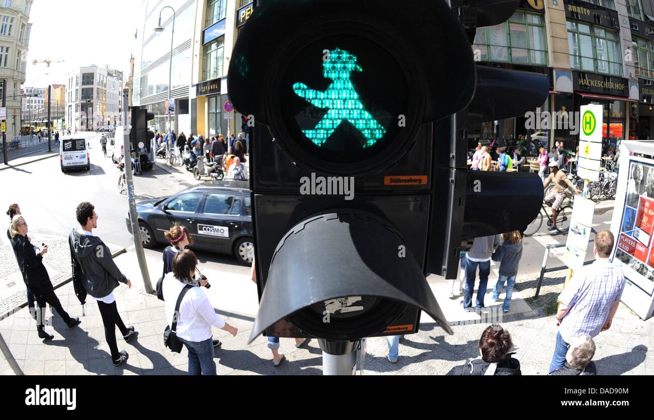 People cross the street under a green Ampelmaennchen (little traffic light man) in Berlin, Germany, 09 August 2011. On 13 October 1961, Karl Peglau presented his traffic light figure at the East German Ministry of Transport and the ampelmaennchen was born, but it took another eight years before the first green figure found its place on a traffic signal in Berlin. Photo: Rainer Jens Stock Photo