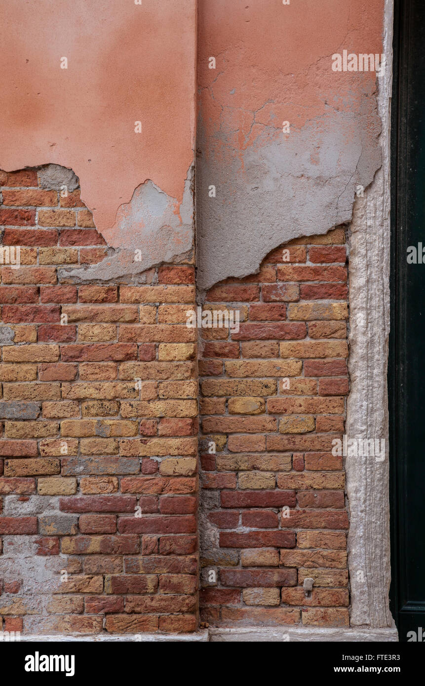 Frontage detail of a decaying building with crumbling pink painted render exposed warm toned red and orange brickwork in Venice, Italy Stock Photo