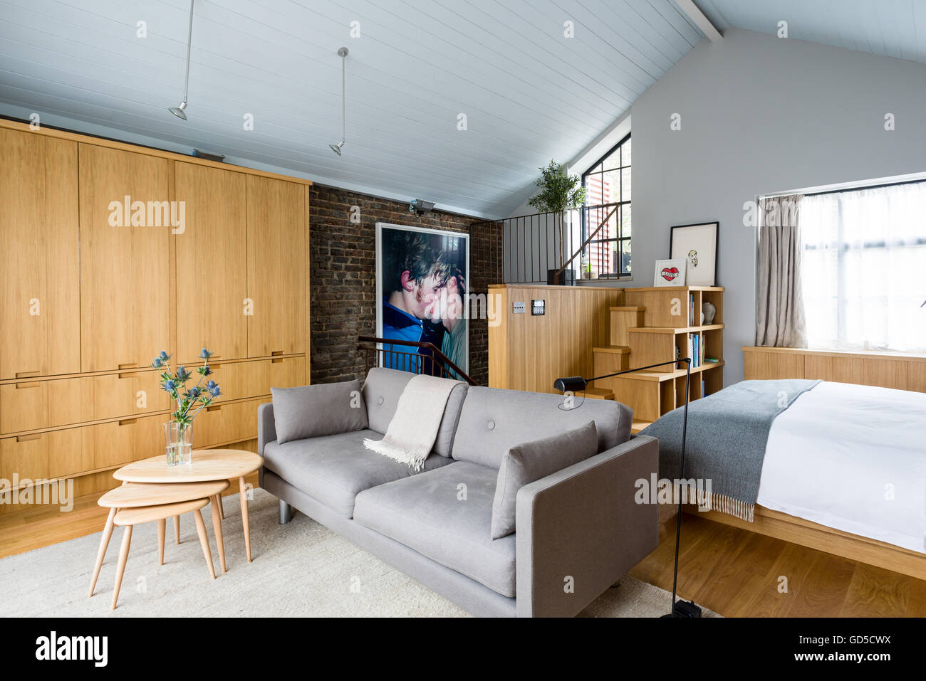 Custom built oak cupboards in bedroom. A Wolfgang Tilmans photograph hangs on the exposed brick wall. The sofa is by Erik Jorgen Stock Photo