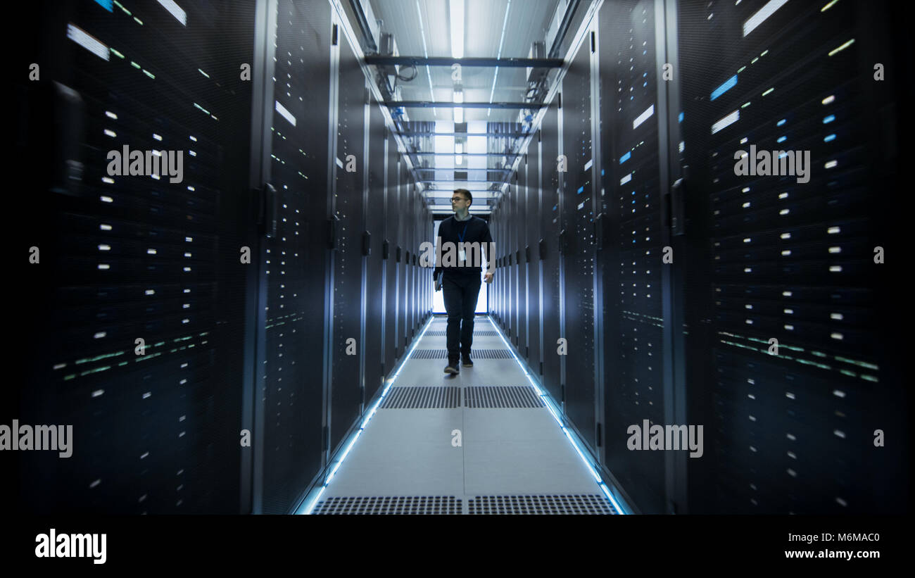 Shot of IT Engineer Walking Through Data Center Corridor with Rows of Rack Servers. Stock Photo