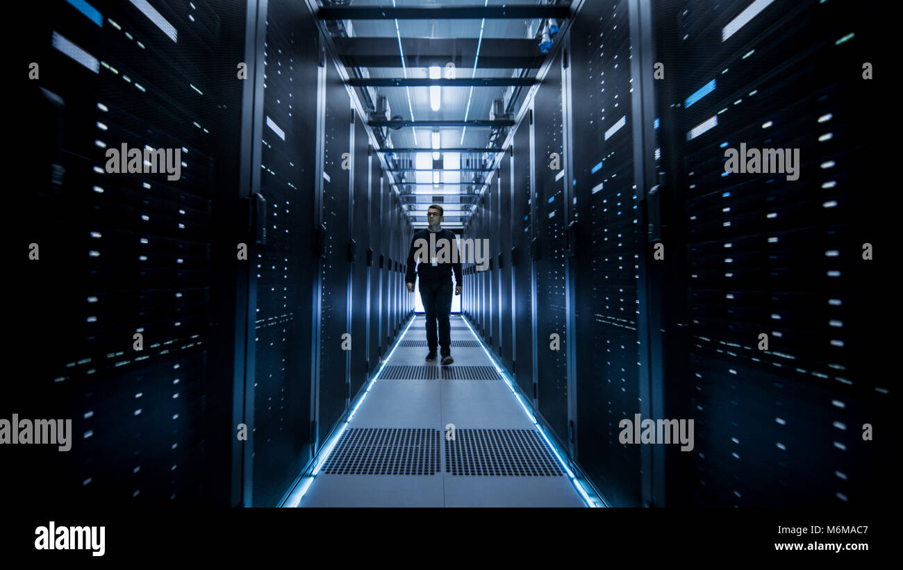 Shot of IT Engineer Walking Through Data Center Corridor with Rows of Rack Servers. Stock Photo