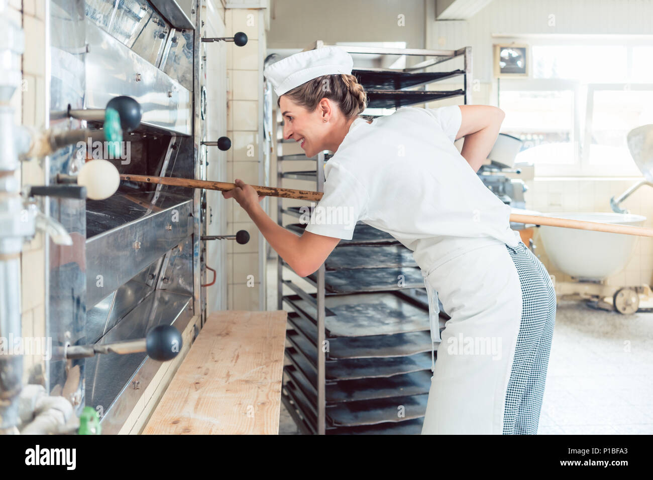 Baker woman getting bread out of bakery oven Stock Photo