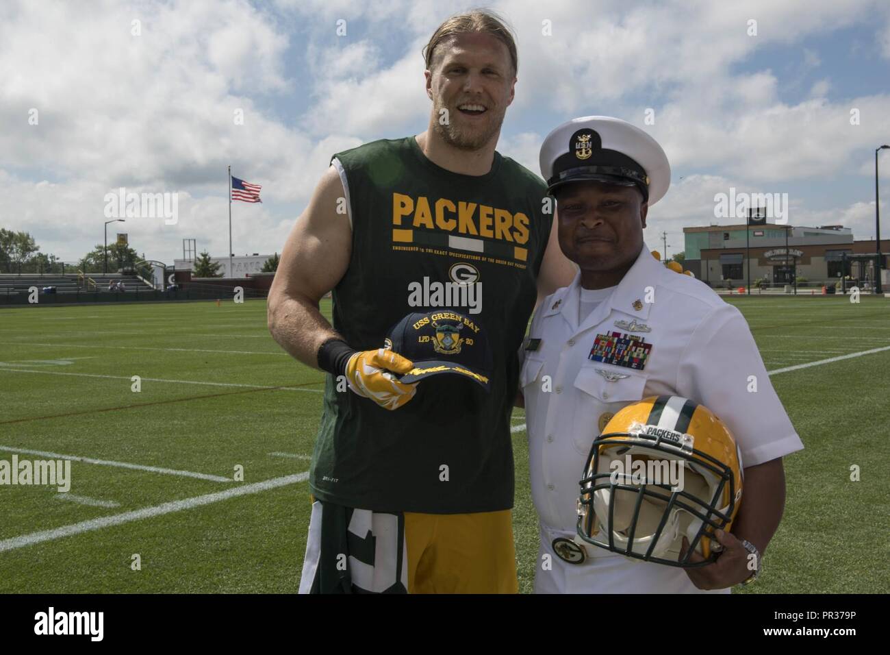 GREEN BAY, Wis. (July 28, 2017) – David Robinson Jr., Command Master Chief, USS Green Bay (LPD 20), presents Green Bay Packers linebacker Clay Matthews III with a ship’s ball cap on the sidelines of the Packers’ practice field during Green Bay/Fox Cities Navy Week. Navy Week programs serve as the U.S. Navy's principal outreach effort into areas of the country that lack a significant Navy presence, helping Americans understand that their Navy is deployed around the world, around the clock, ready to defend America at all times. Stock Photo