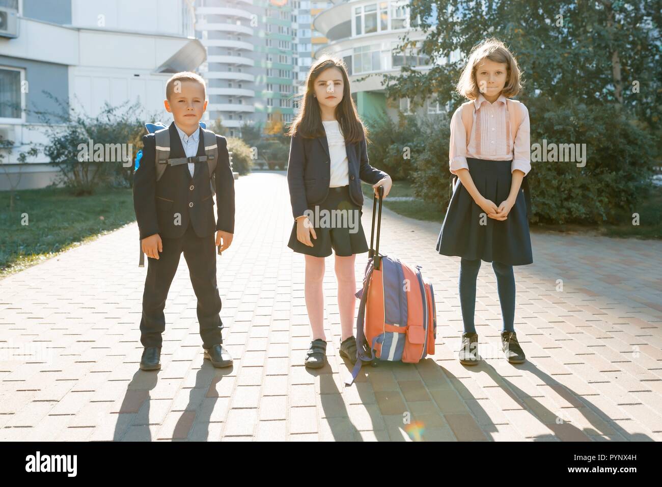 Outdoor portrait of smiling schoolchildren in elementary school. A group of kids with backpacks are having fun, talking. Education, friendship, techno Stock Photo