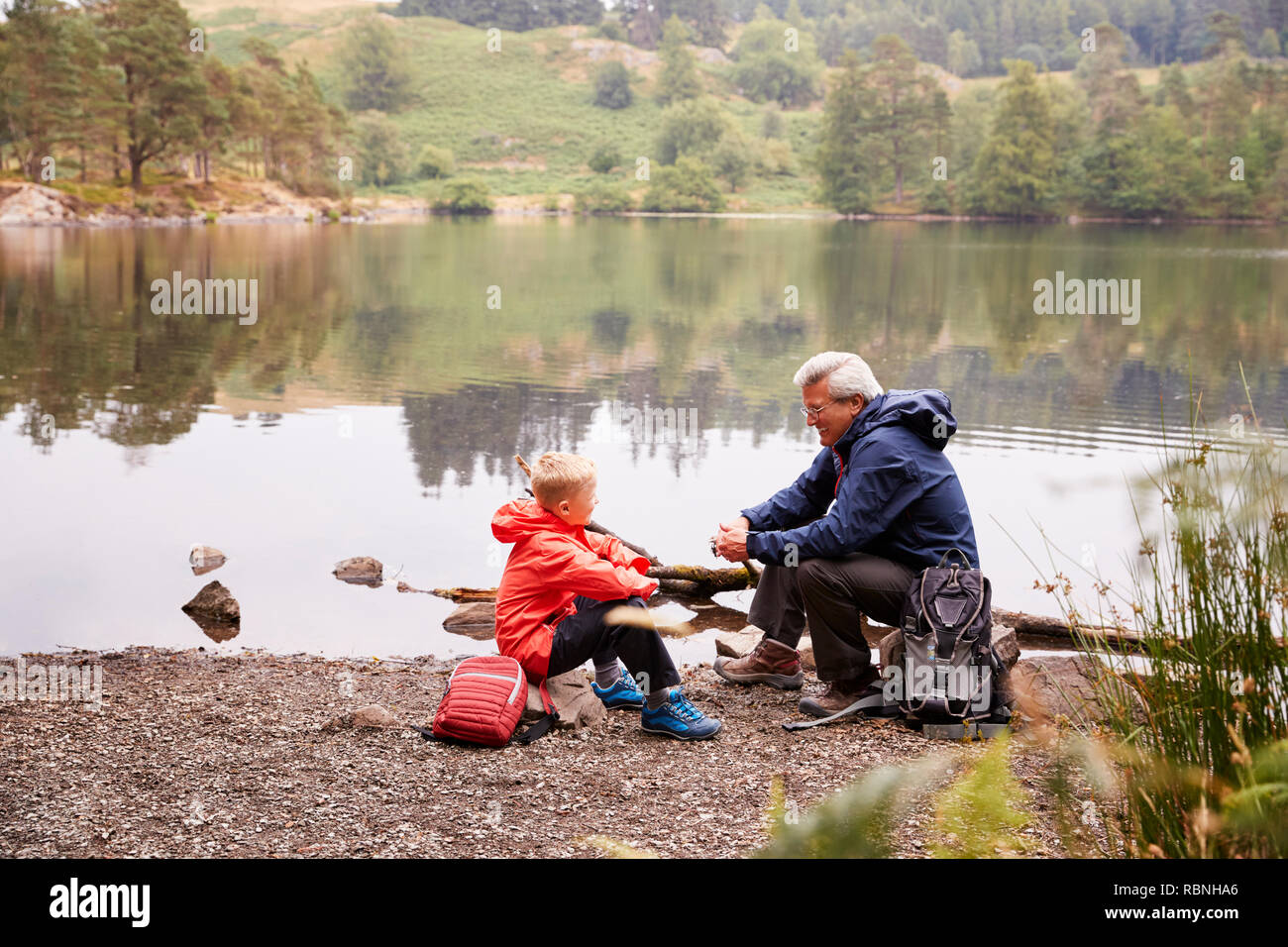 Grandfather and grandson sitting at the shore of a lake talking, elevated view, Lake District, UK Stock Photo