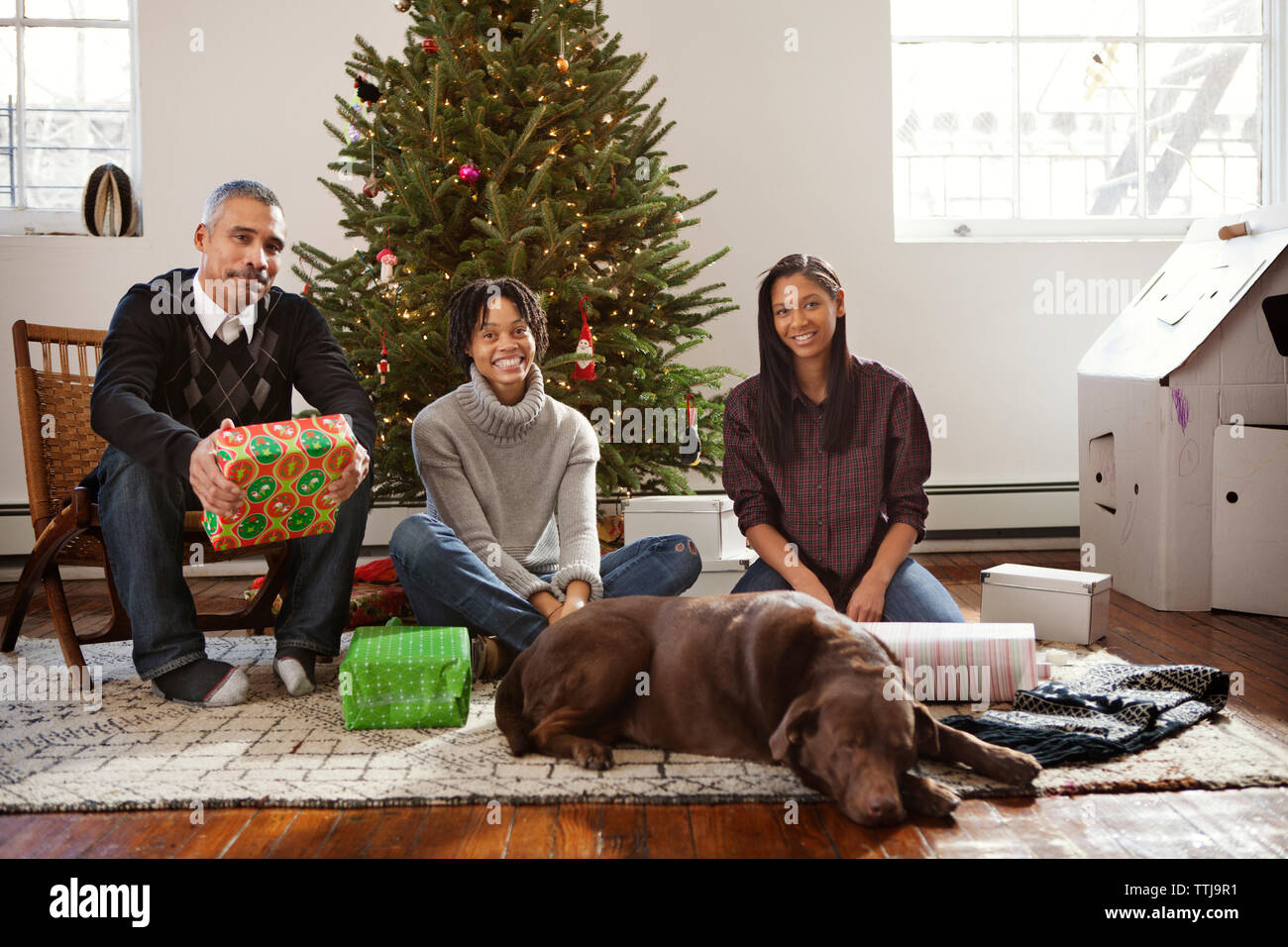 Happy family with dog sitting by christmas tree at home Stock Photo