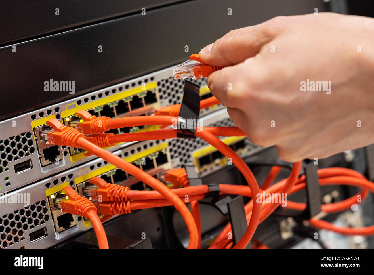 Male IT Engineer Plugging Network Cable In Router in Datacenter Stock Photo