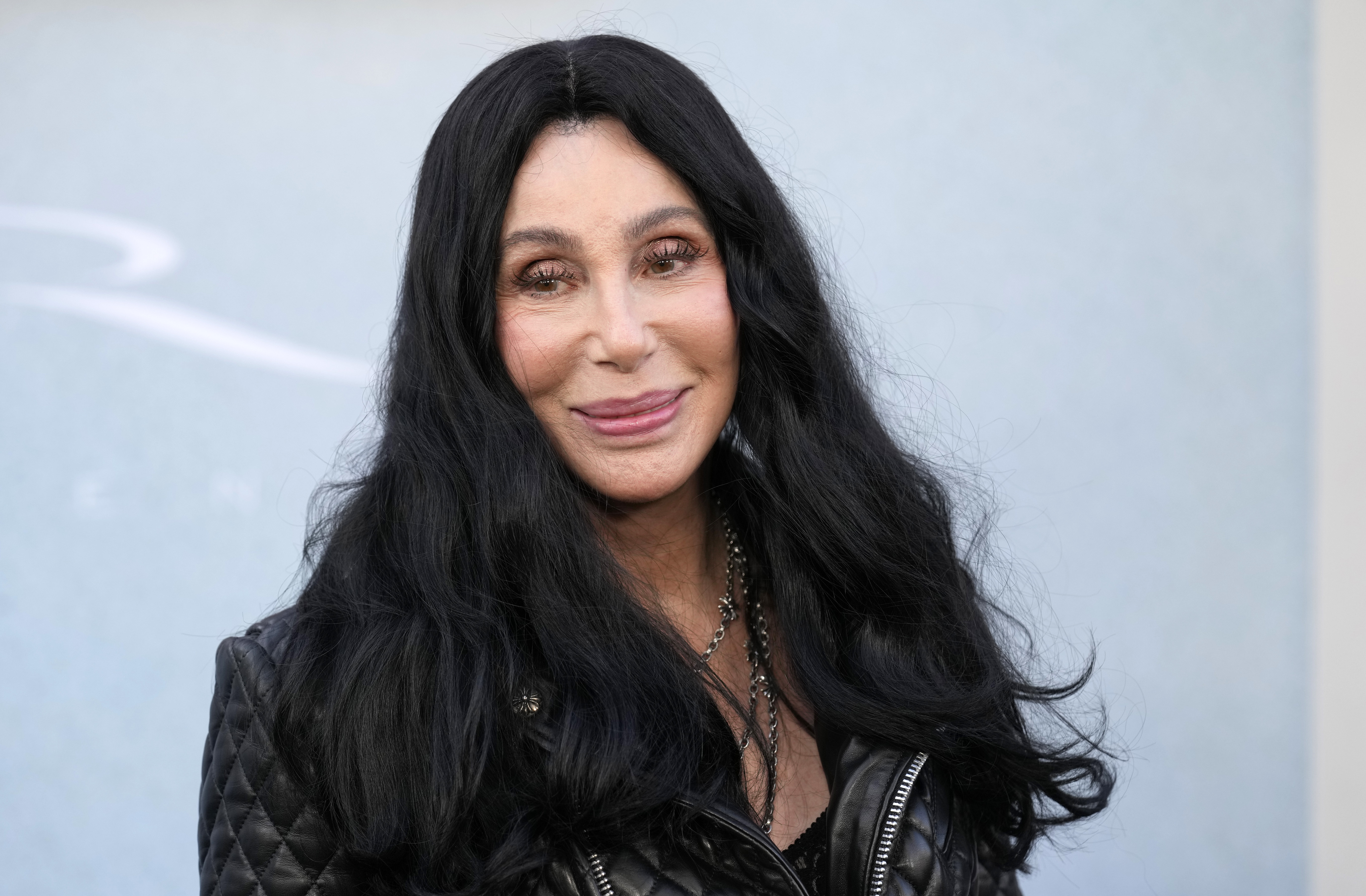 Cher smiles with her long dark hair parted in the middle while wearing a black leather jacket