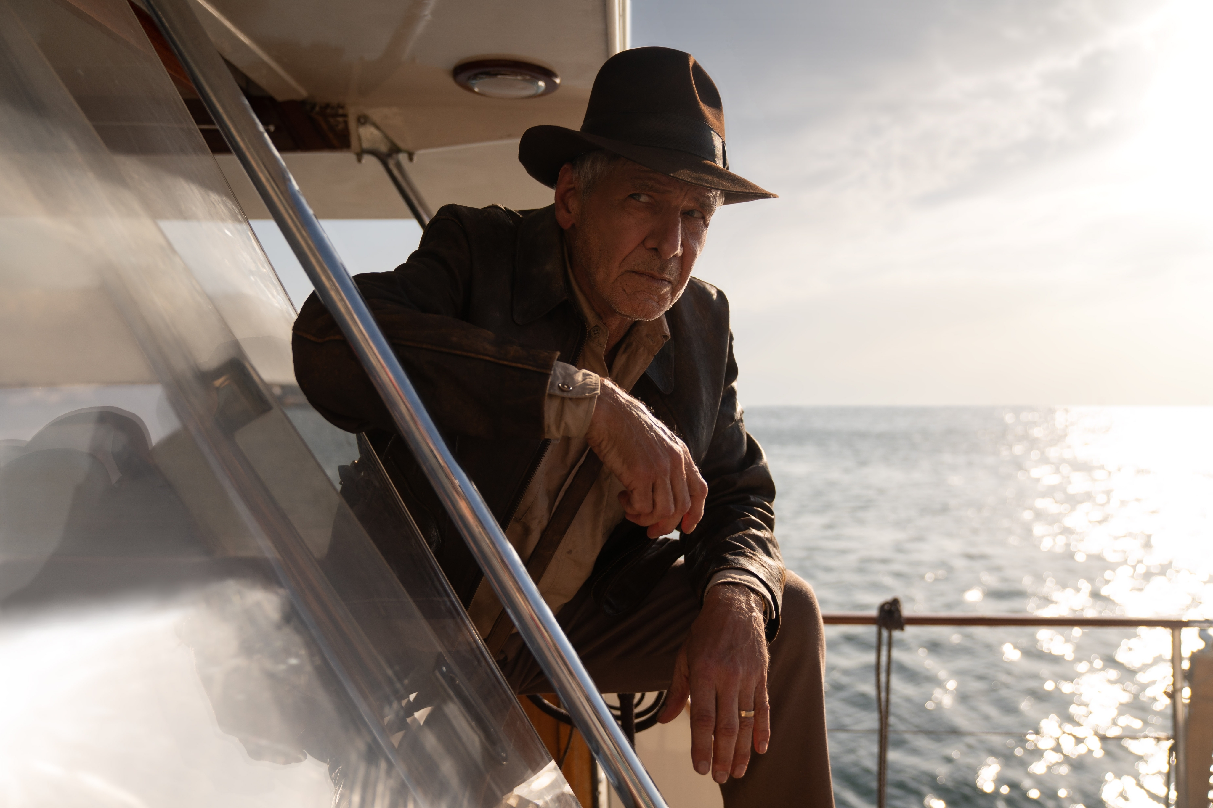 Harrison Ford as Indiana Jones leaning over a railing on a ship with the water gleaming behind him.