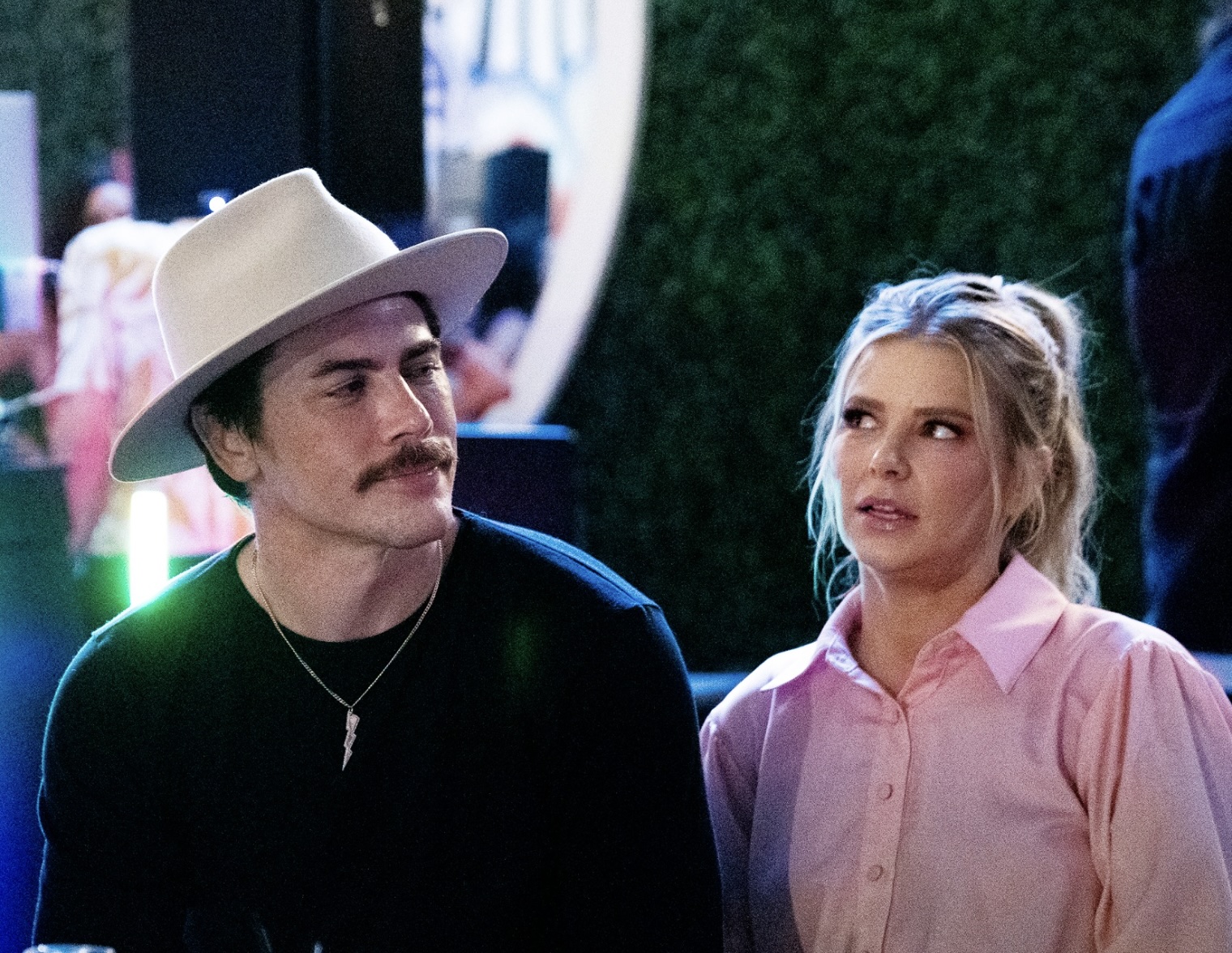 Tom Sandoval (L) in a black shirt and tan hat and Ariana Madix in a pink button-up blouse.
