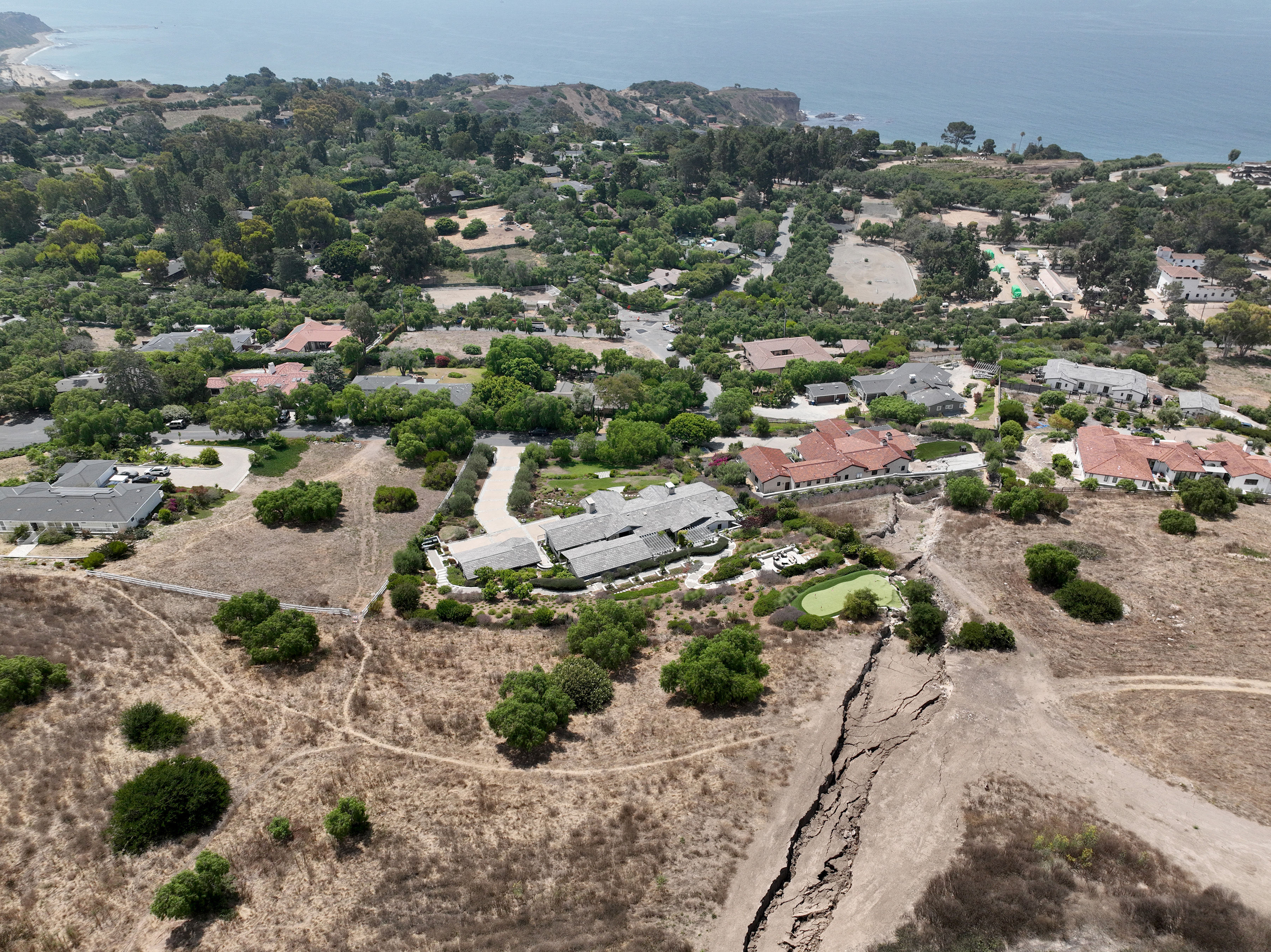 Rancho Palos Verdes, CA - August 01: An aerial view of a large fissure that has opened up since February, damaging a Portuguese Bend putting green and home after last winter's heavy rain in Rancho Palos Verdes Thursday, Aug. 1, 2024. Due to continual land movement, the Portuguese bend neighborhood in Rancho Palos Verde could face power shut off. Mike Hong, whose home neighbors a large fissure that has been getting larger and deeper since February, when the area was inundated with heavy rains. He says that water is draining from Rolling Hills homes into Altamira Canyon and directly flowing into the earth and not into the ocean, which is part of a proposed drainage plan. He says lining the canyon would help as rain saturation is one of the contributing factors to movement in the area. The fissure also passes through and through the Palos Verdes Nature Preserve. (Allen J. Schaben / Los Angeles Times)