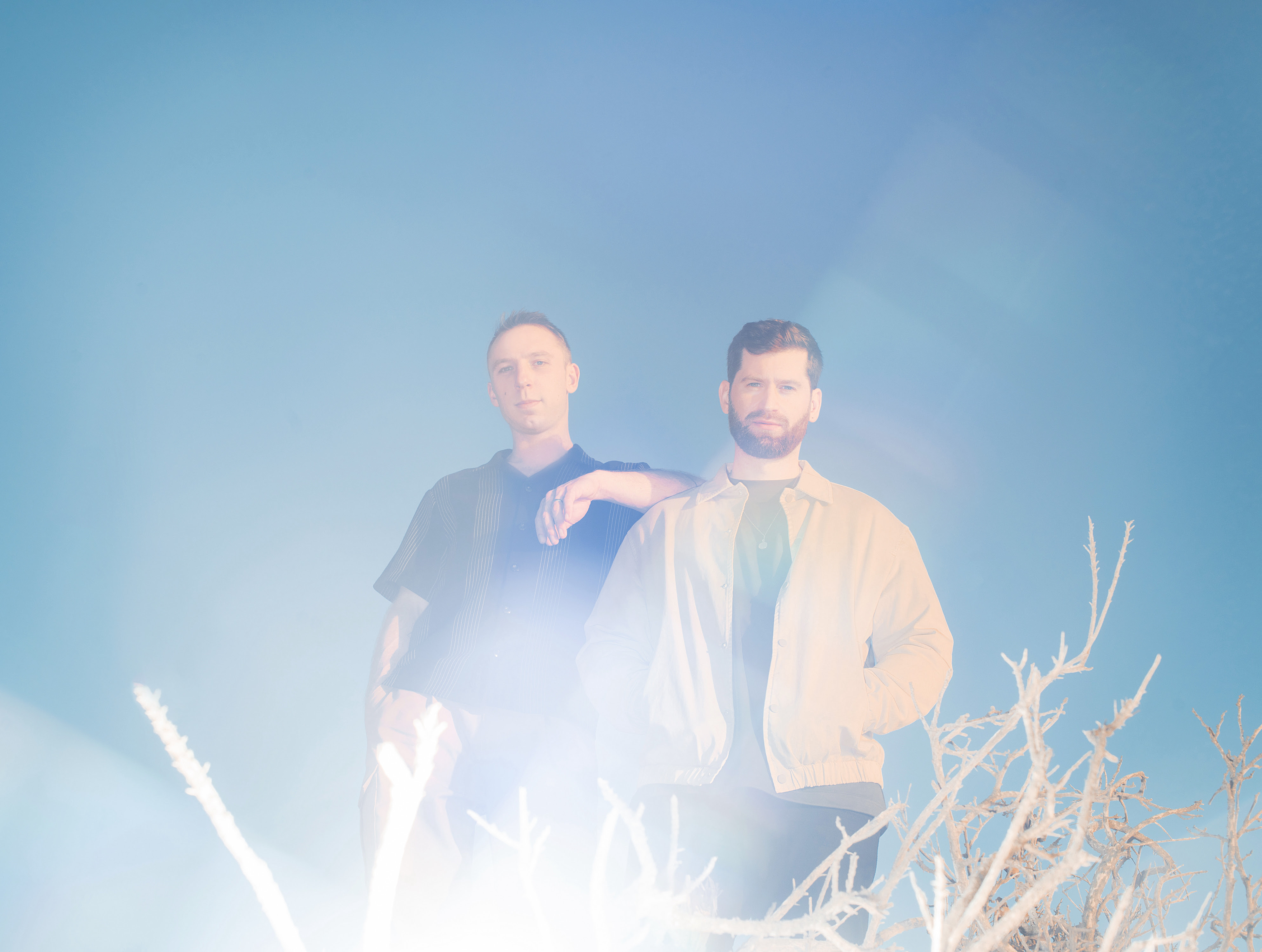 Clayton Knight and Harrison Mills stand outside under a blue sky with brush below them