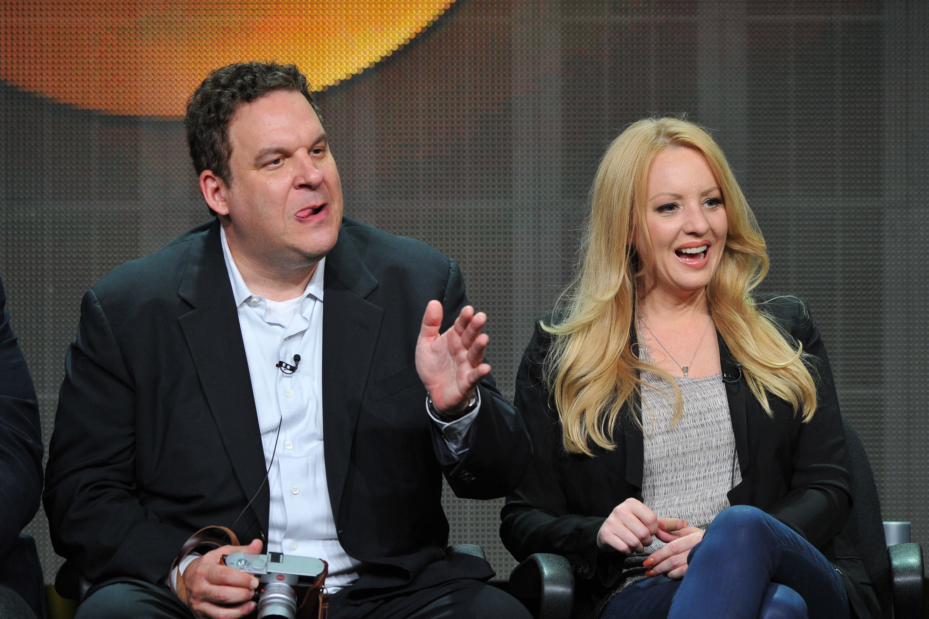 A man with brown hair in a suit gestures with his hand while sitting next to a woman with long blond hair in a blazer