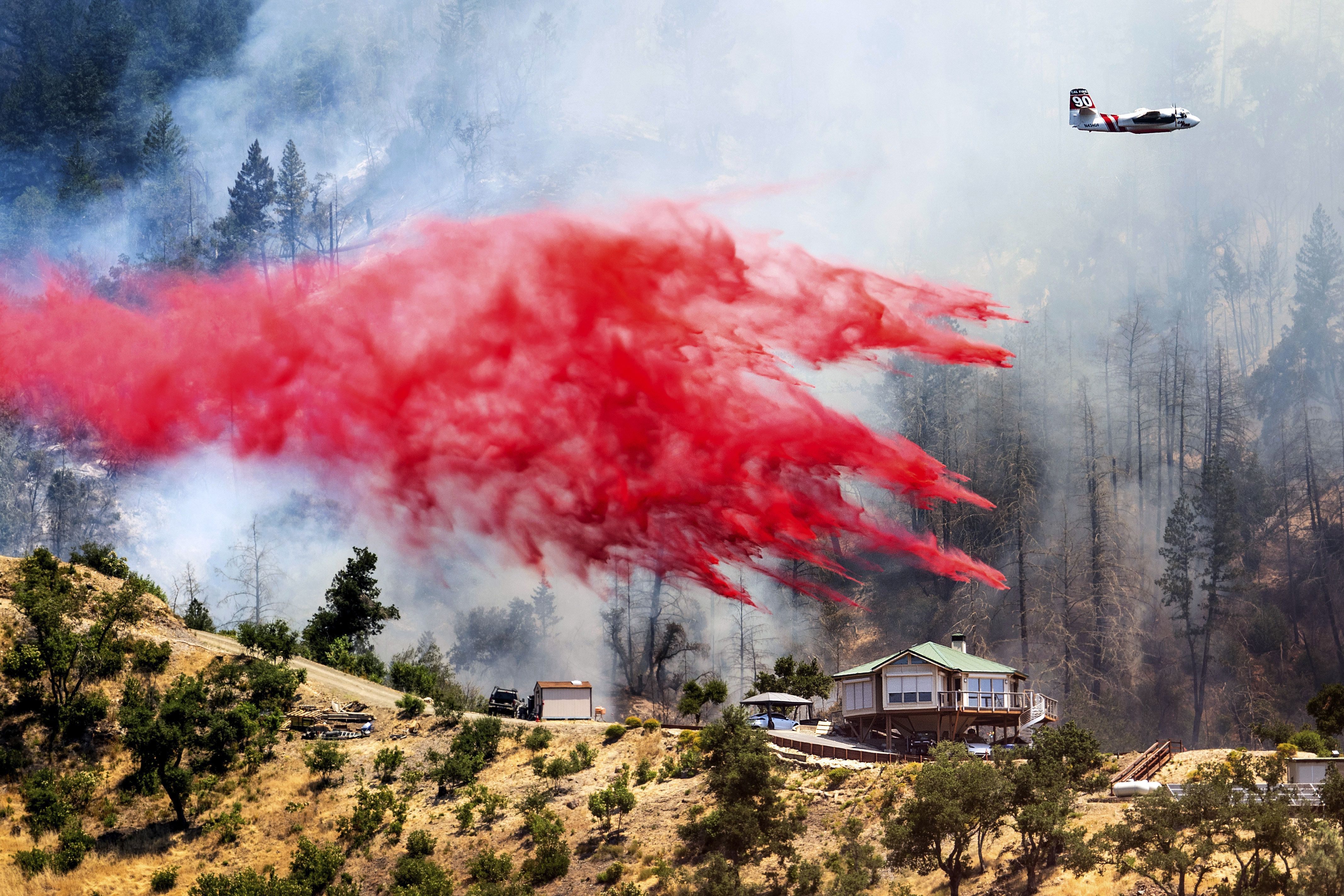 An air tanker drops retardant behind a home while battling the Toll Fire near Calistoga, Calif., Tuesday, July 2, 2024. An extended heatwave blanketing Northern California has resulted in red flag fire warnings and power shutoffs. (AP Photo/Noah Berger)