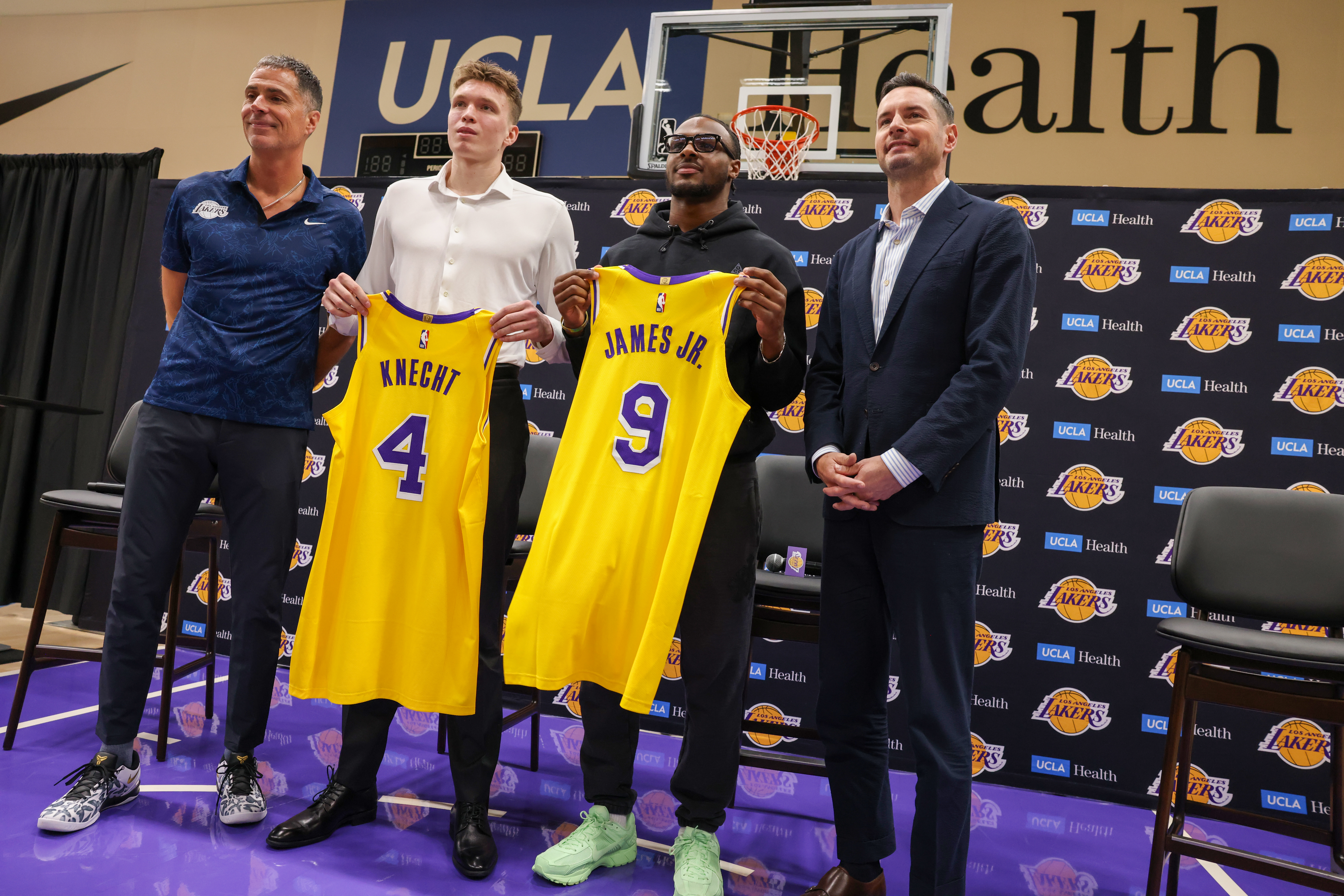 Lakers draft picks Dalton Knecht and Bronny James hold up jerseys while standing beside Rob Pelinka and JJ Redick