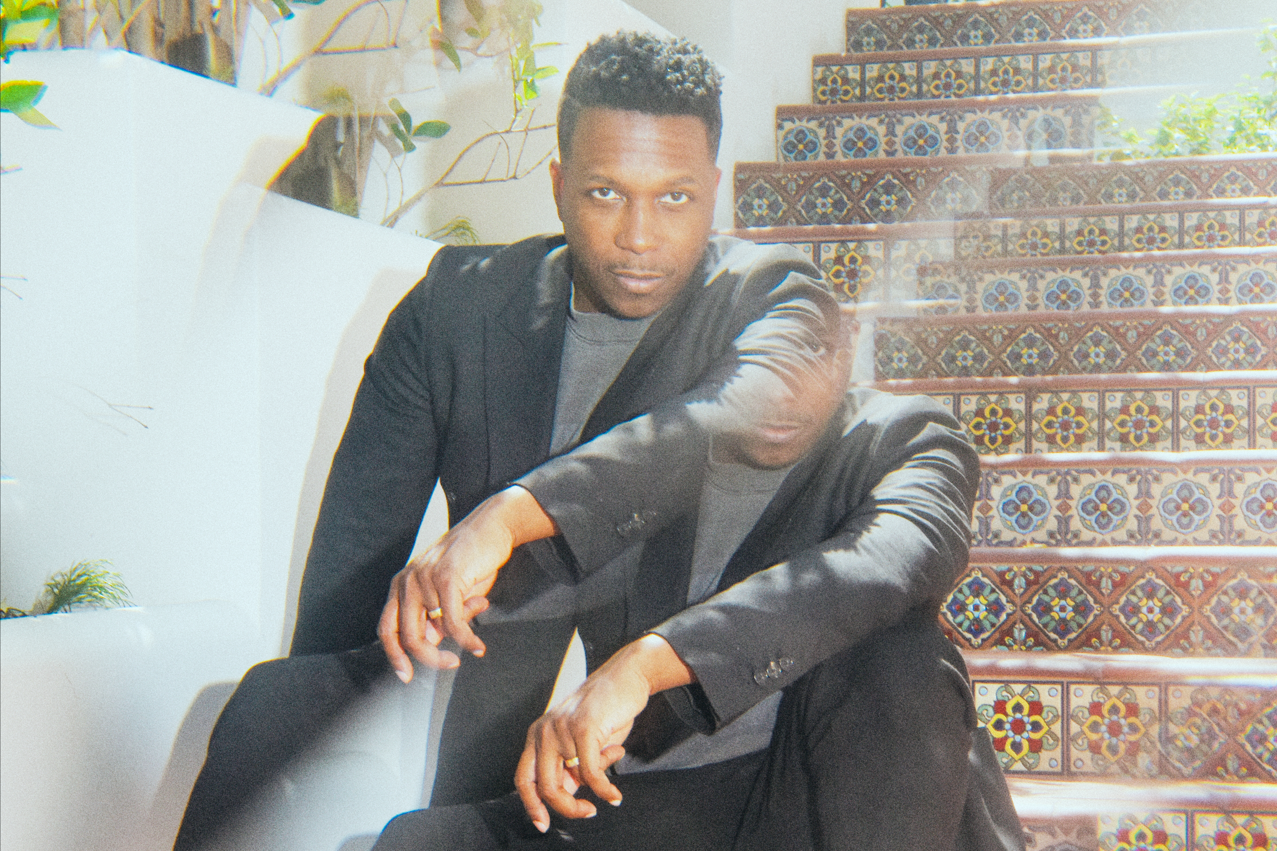 A double exposure of Leslie Odom Jr. sitting on stairs.