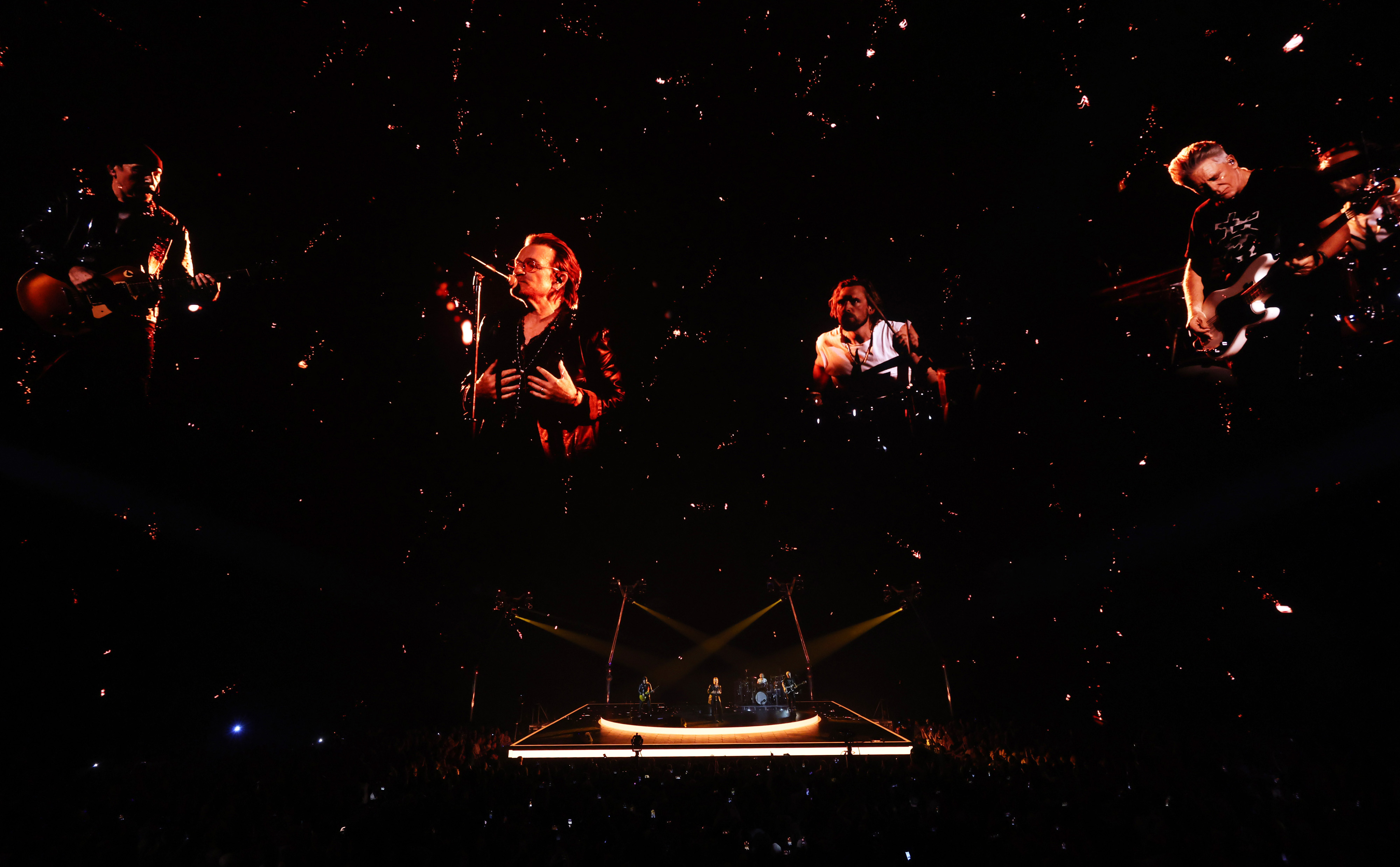 U2 performs in front of a black background with pinpoints of light.