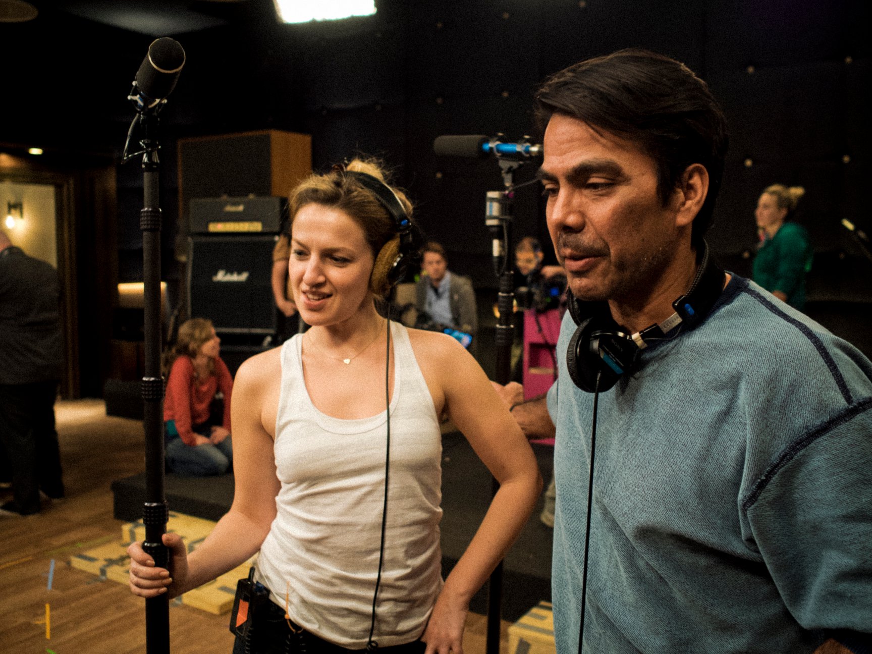 Heather Fink, in a white tank top and headphones, holds a boom mic on set.