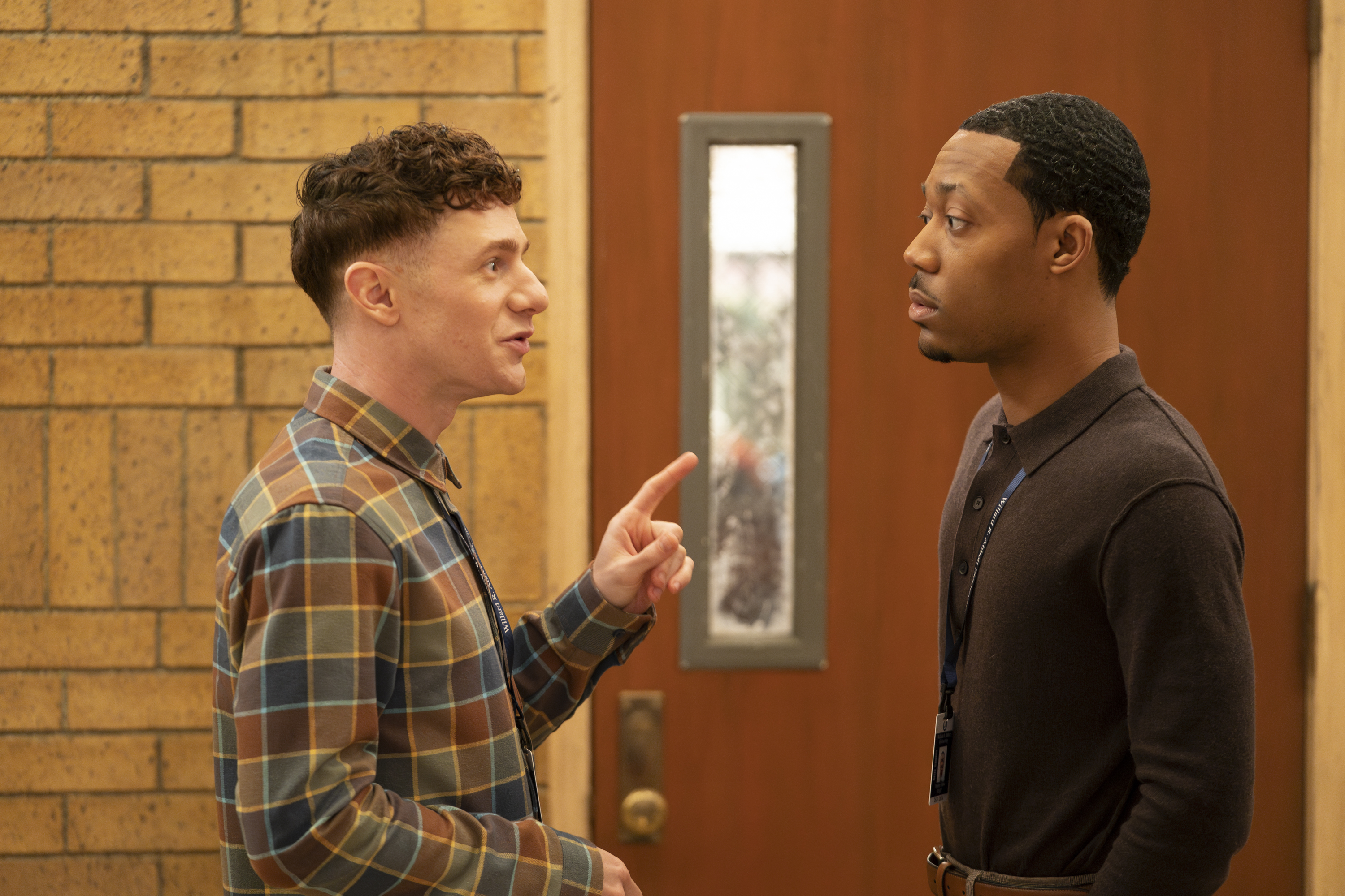 Two male schoolteachers talk in a corridor.