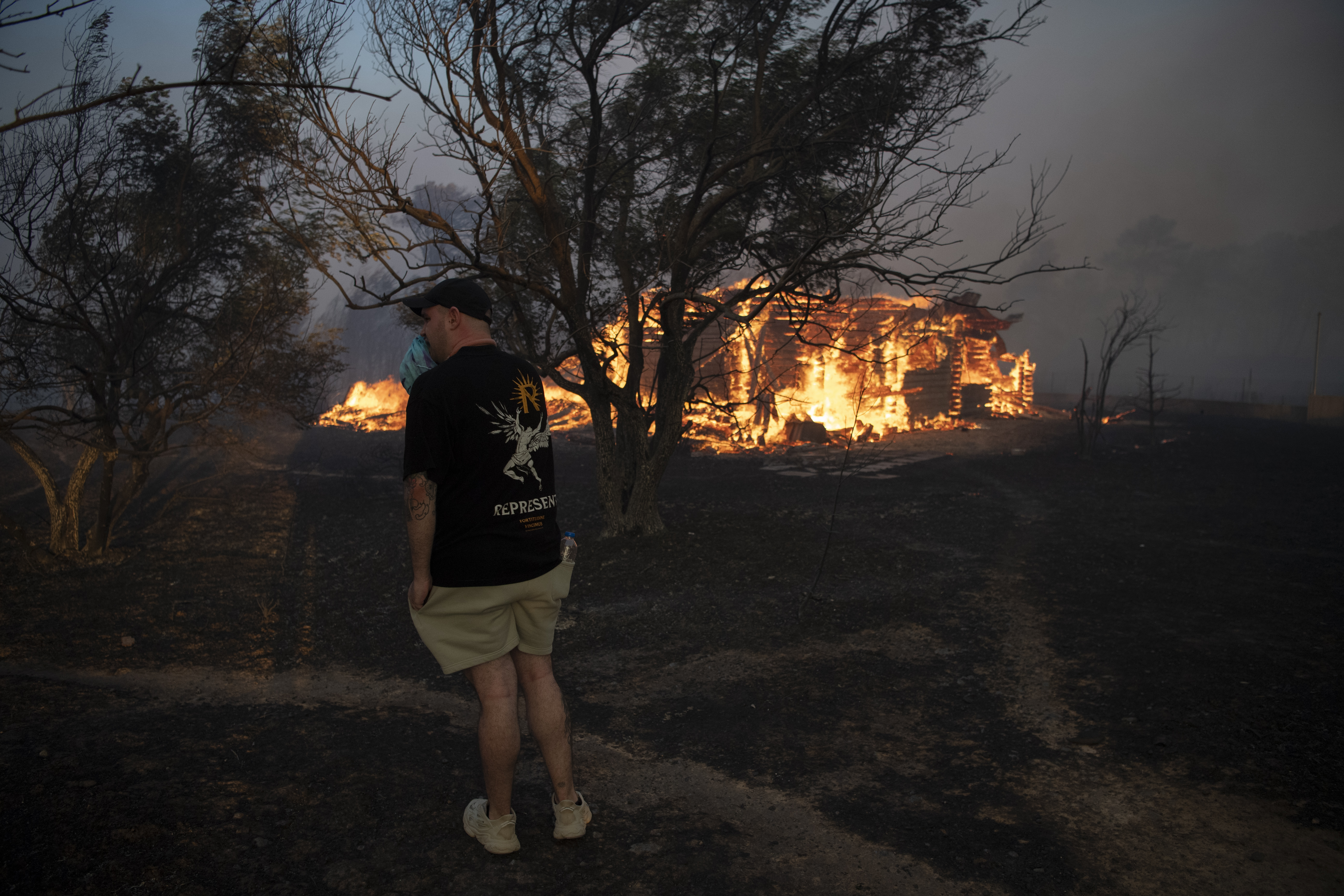 A man reacts as a house is on fire in Varnava village during a wildfire, north of Athens, Greece, Sunday, Aug. 11, 2024, with many regions of the country on high alert due to high temperatures and wind speeds. (AP Photo/Michael Varaklas)