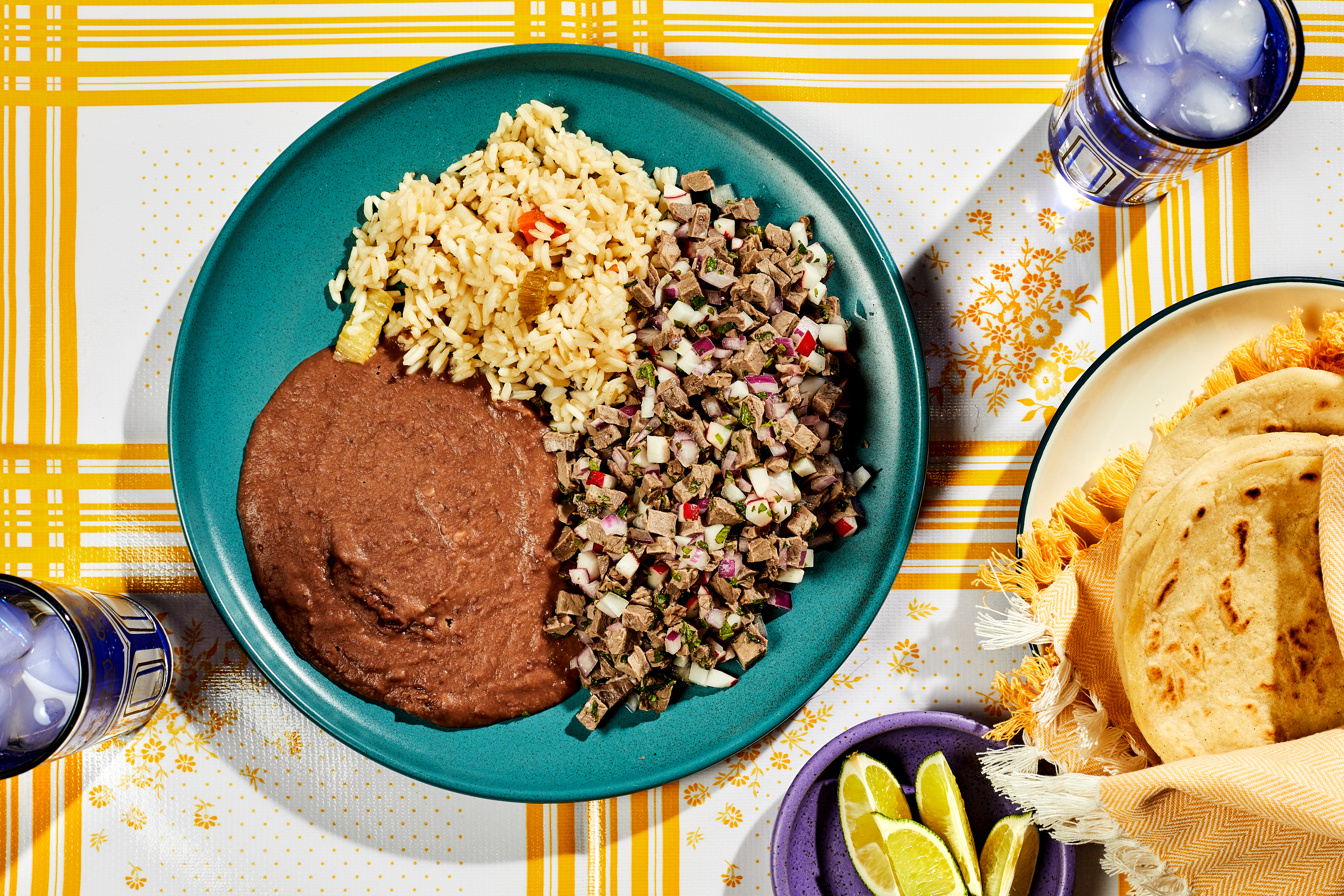 A plate of Salpicon de Res with rice and beans next to a plate of tortillas