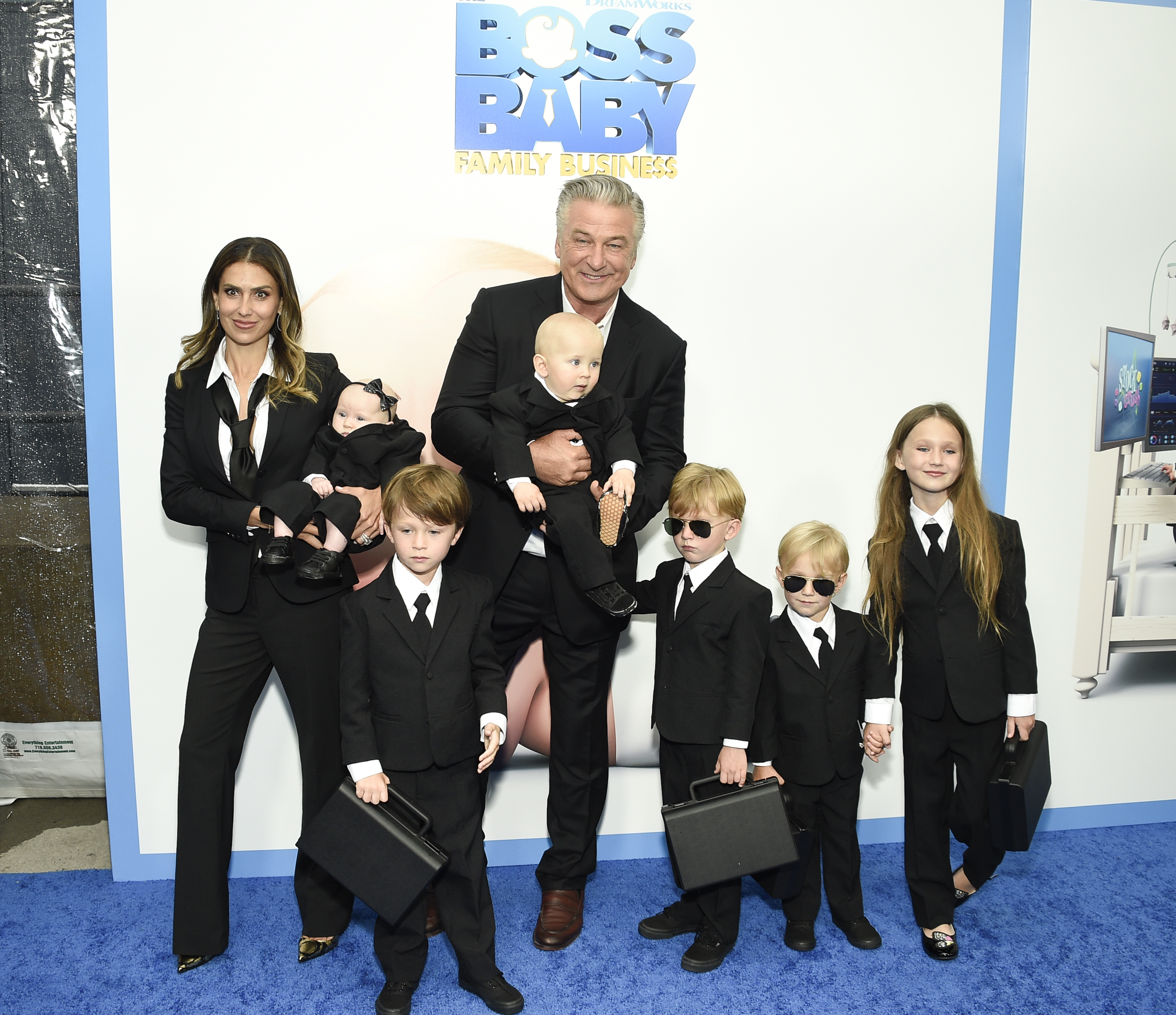 A family of six poses in suit on a blue carpet for a movie premiere