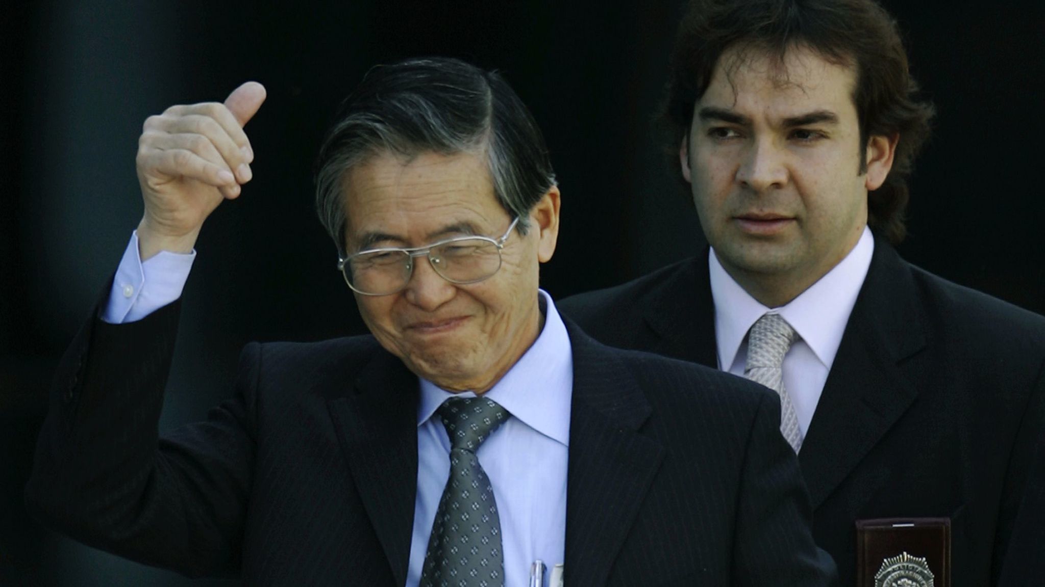 Flanked by Chilean investigative police, former Peruvian President Alberto Fujimori gives a "thumbsup" sign as he leaves the Chilean investigative police academy in Santiago, Chile, Monday, Nov. 7, 2005. Fujimori was arrested in Chile Monday on charges at home involving corruption and massacres, as he attempted to return to Peru to run for reelection after five years as a protected exile in Japan. (AP Photo/Roberto Candia)