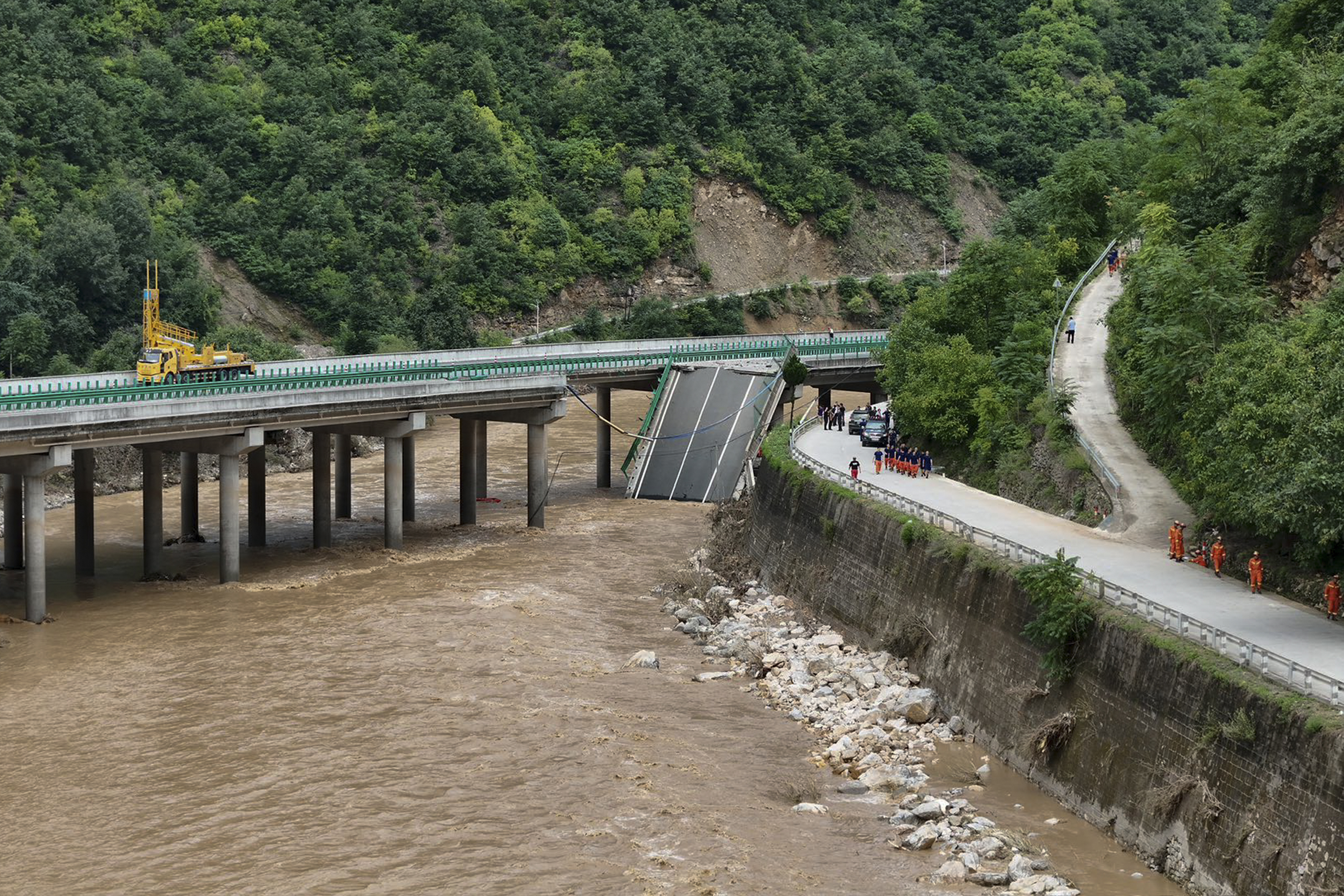 In this photo released by Xinhua News Agency, rescuers work near a collapsed bridge in Zhashui County in Shangluo City, northwest China's Shaanxi Province, Saturday, July 20, 2024. Chinese authorities say several people have died and more than dozen are missing in the partial collapse of a highway bridge in the northwest of the country following heavy storms and flooding. A similar number are missing in the southwest after dozens of houses were destroyed by storms. (Zhao Yingbo/Xinhua via AP)