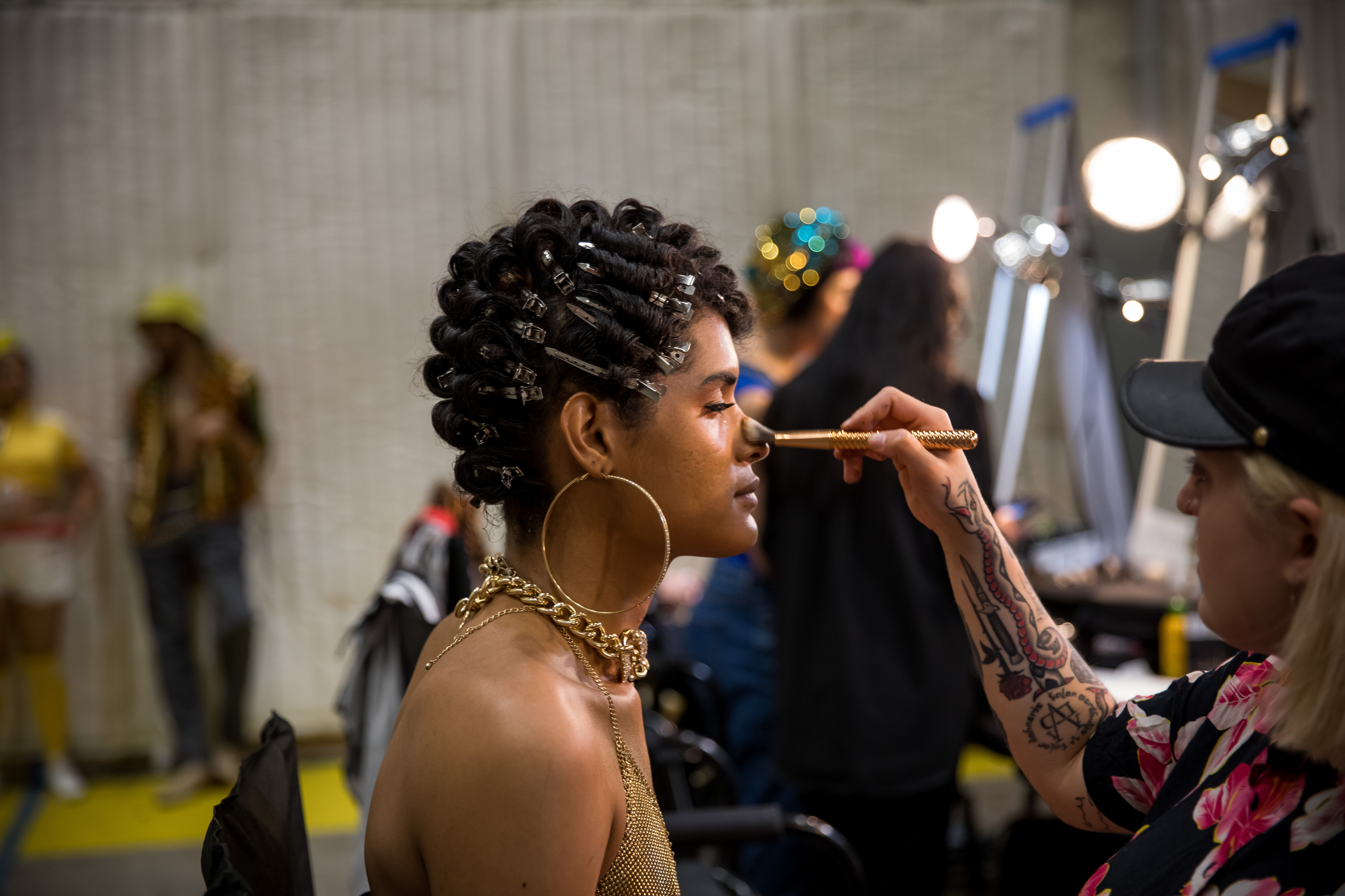 A makeup artist brushes makeup onto a performer's face in a green room behind the scenes of a TV production.