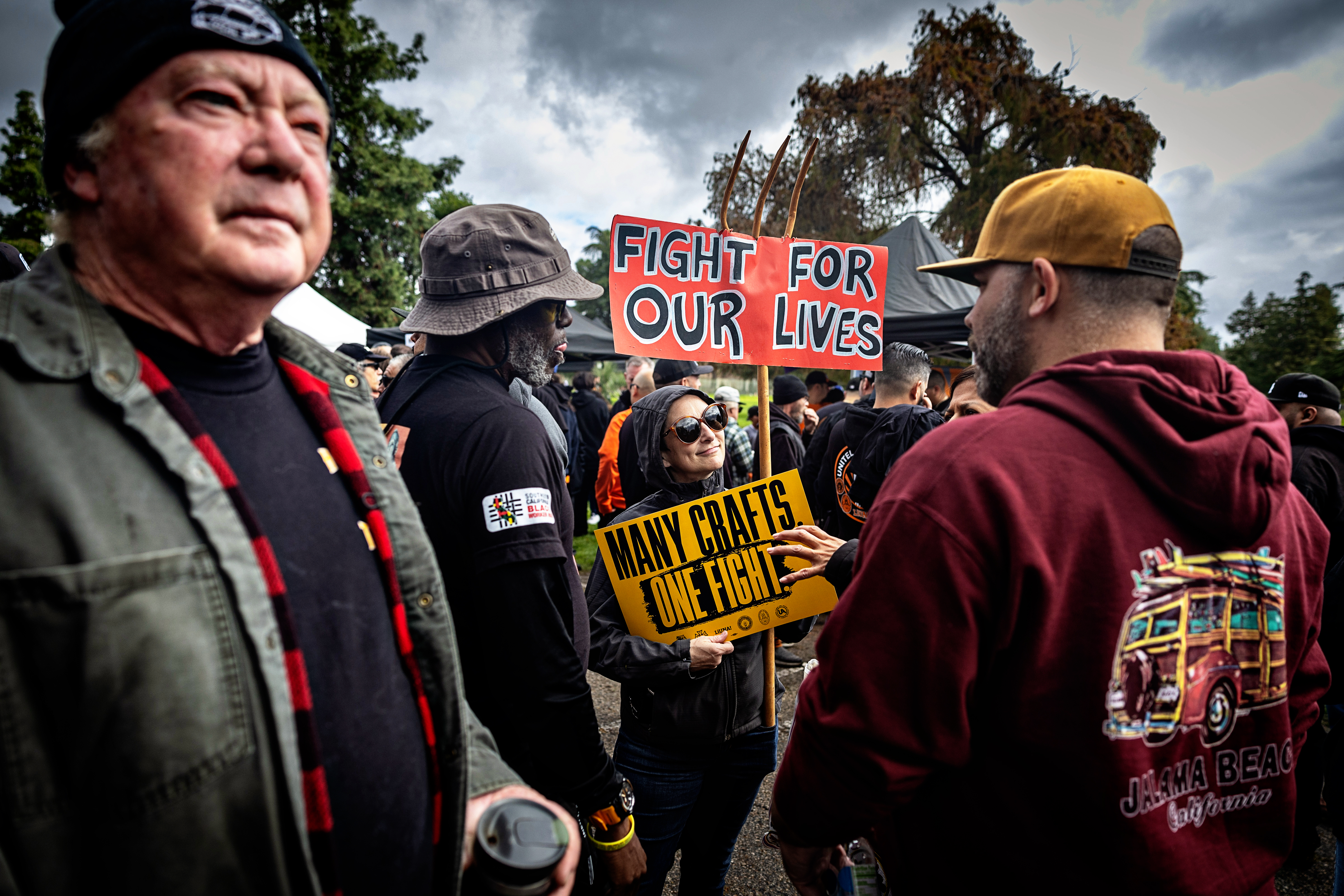 A person carrying picket signs that read "Fight for our lives" and "Many crafts, one fight" amid a crowd of people