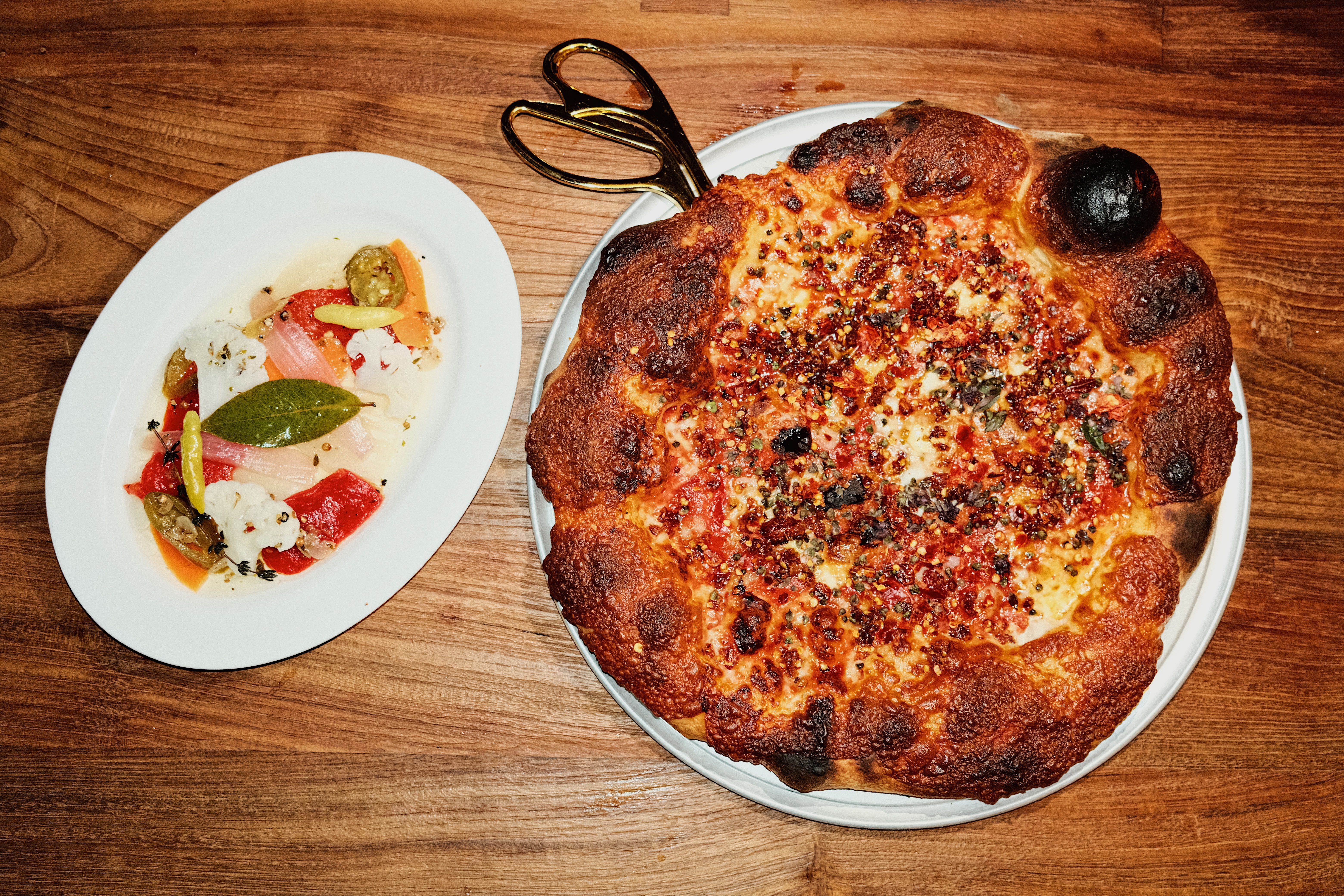 A wide overhead photo of the chile-flecked Hail Satan pizza at Leopardo. Scissors and a side of giardiniera are at the side.