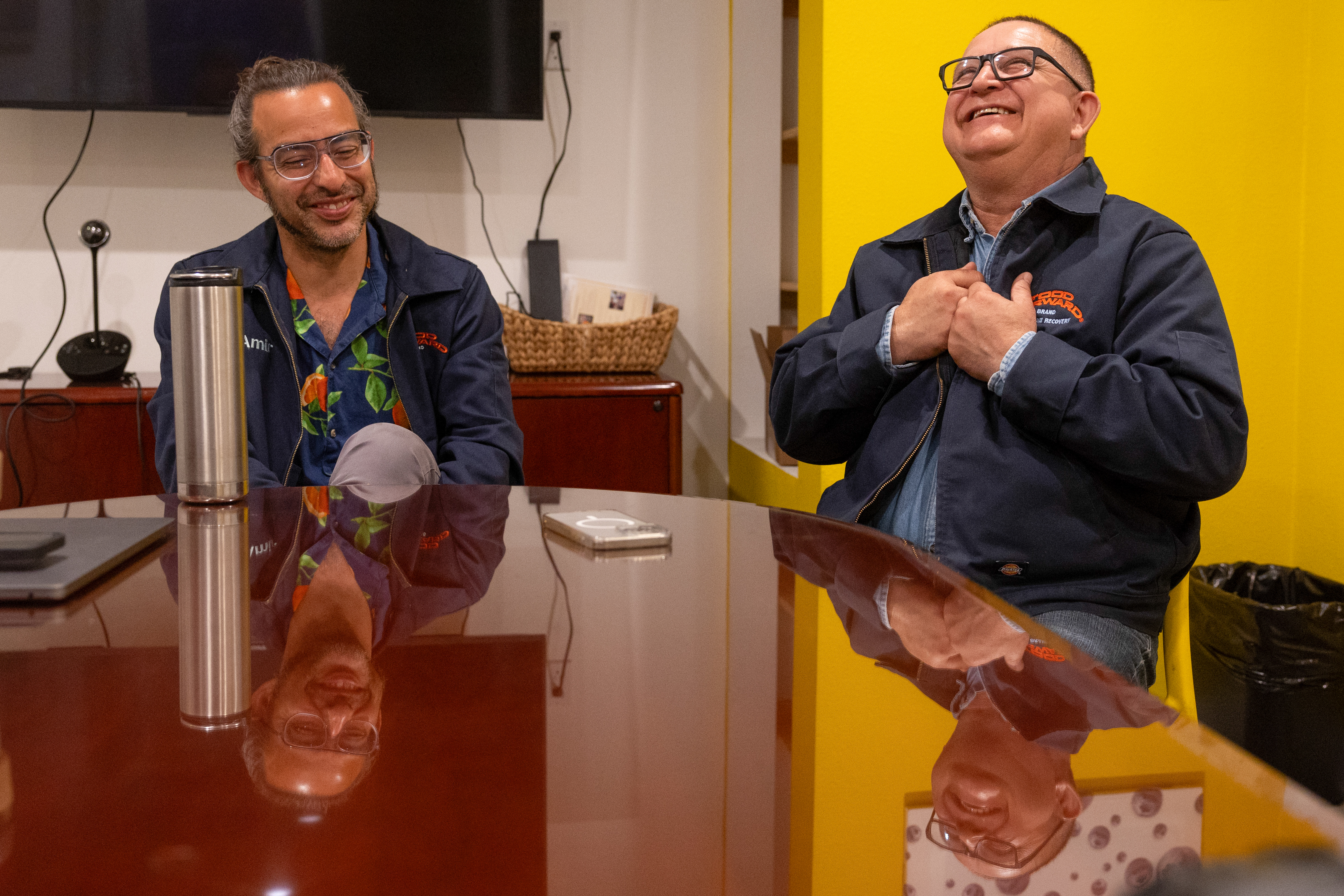 Two men sit at a conference table laughing.