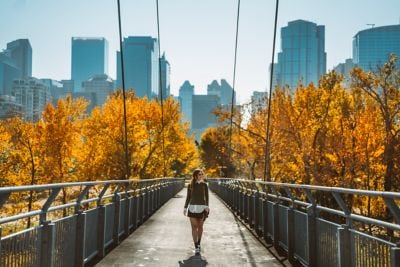 A woman crossing a bridge around fall foliage.