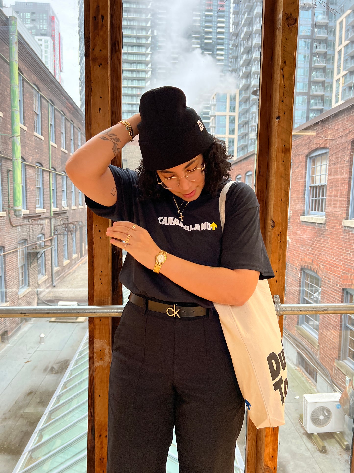 Noor models some Canadaland merch. The Duly Toted tote bag is on her shoulder, giving the viewer an idea of size.