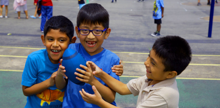 Three boys holding football on playground