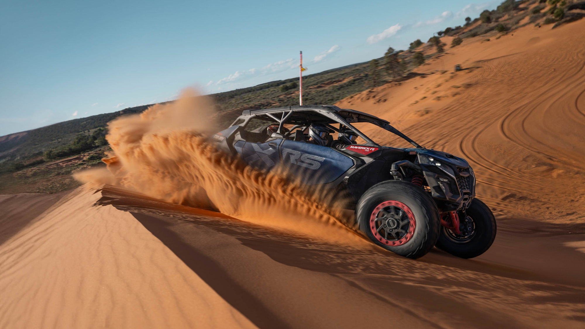 A Can-Am Maverick R X MR 2025 driving at full speed through orange sand dune