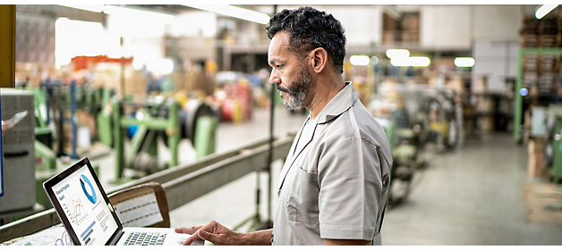 Homem a trabalhar num computador portátil num ambiente industrial.