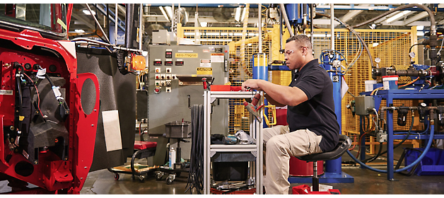 A worker inspects a component at an industrial manufacturing station.