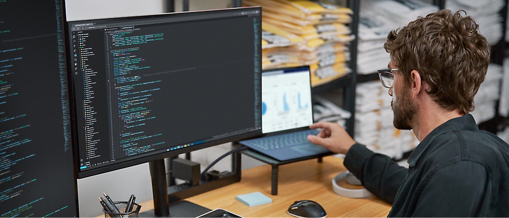 A man is sitting in front of multiple screens and working