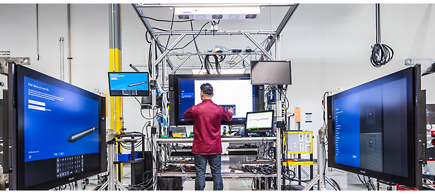 Um técnico a trabalhar em equipamento num laboratório de alta tecnologia rodeado de grandes monitores.