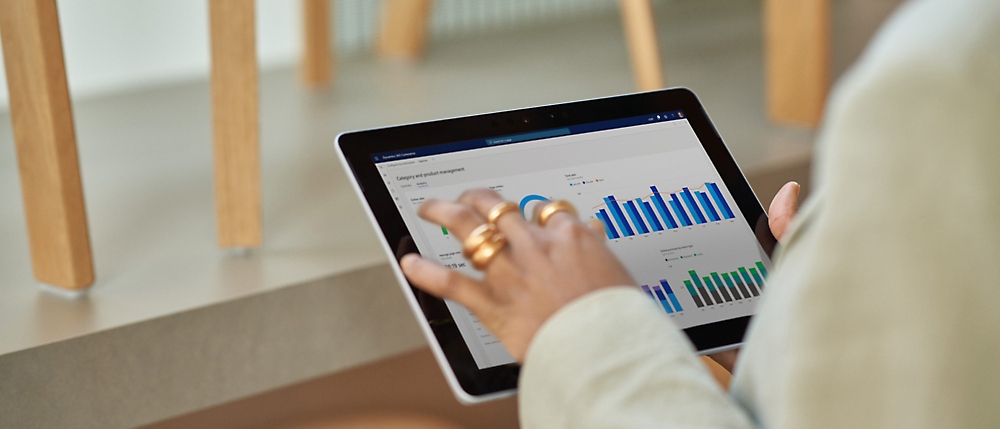 Person analyzing financial charts on a tablet while sitting at a wooden table, focusing on the screen.