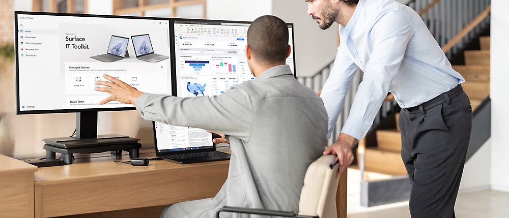 Two professionals discussing over computer screens in a modern office setting.